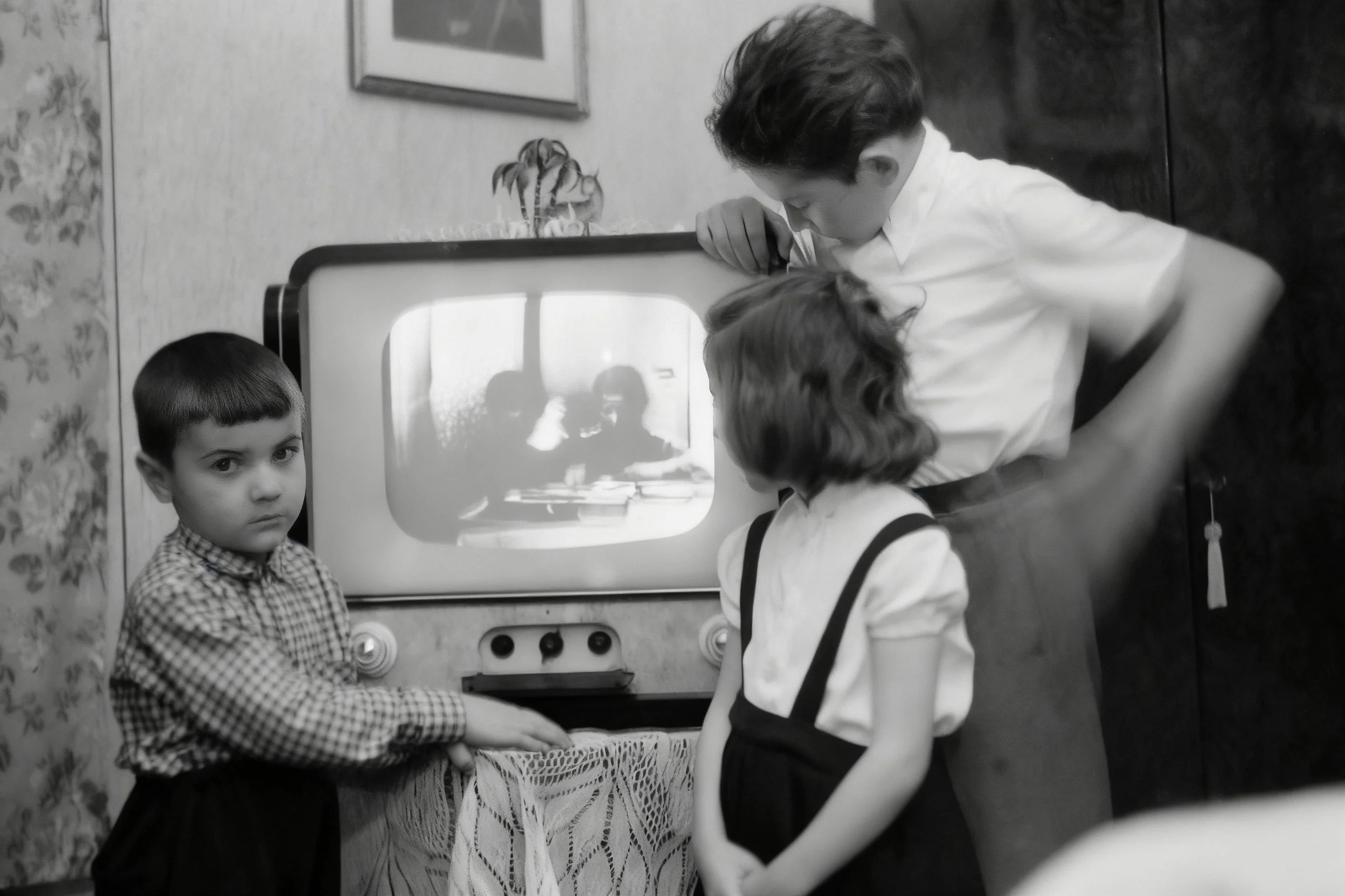 Black-and-white photograph of three children gathered around a television in a living room.