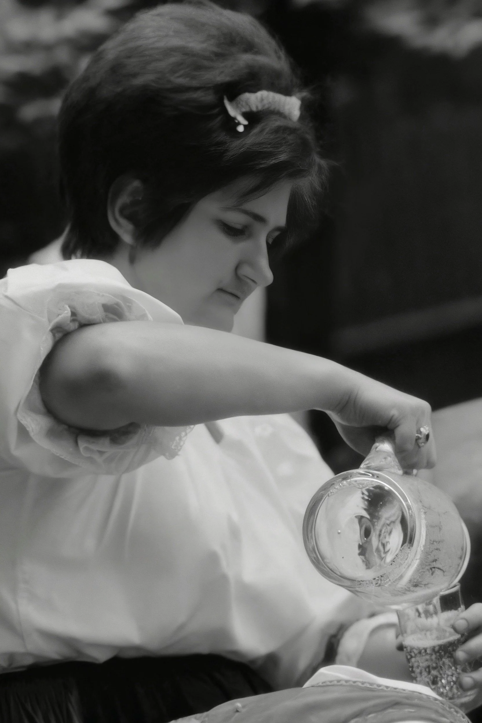 Black-and-white photograph of a woman pouring a drink from a glass pitcher.