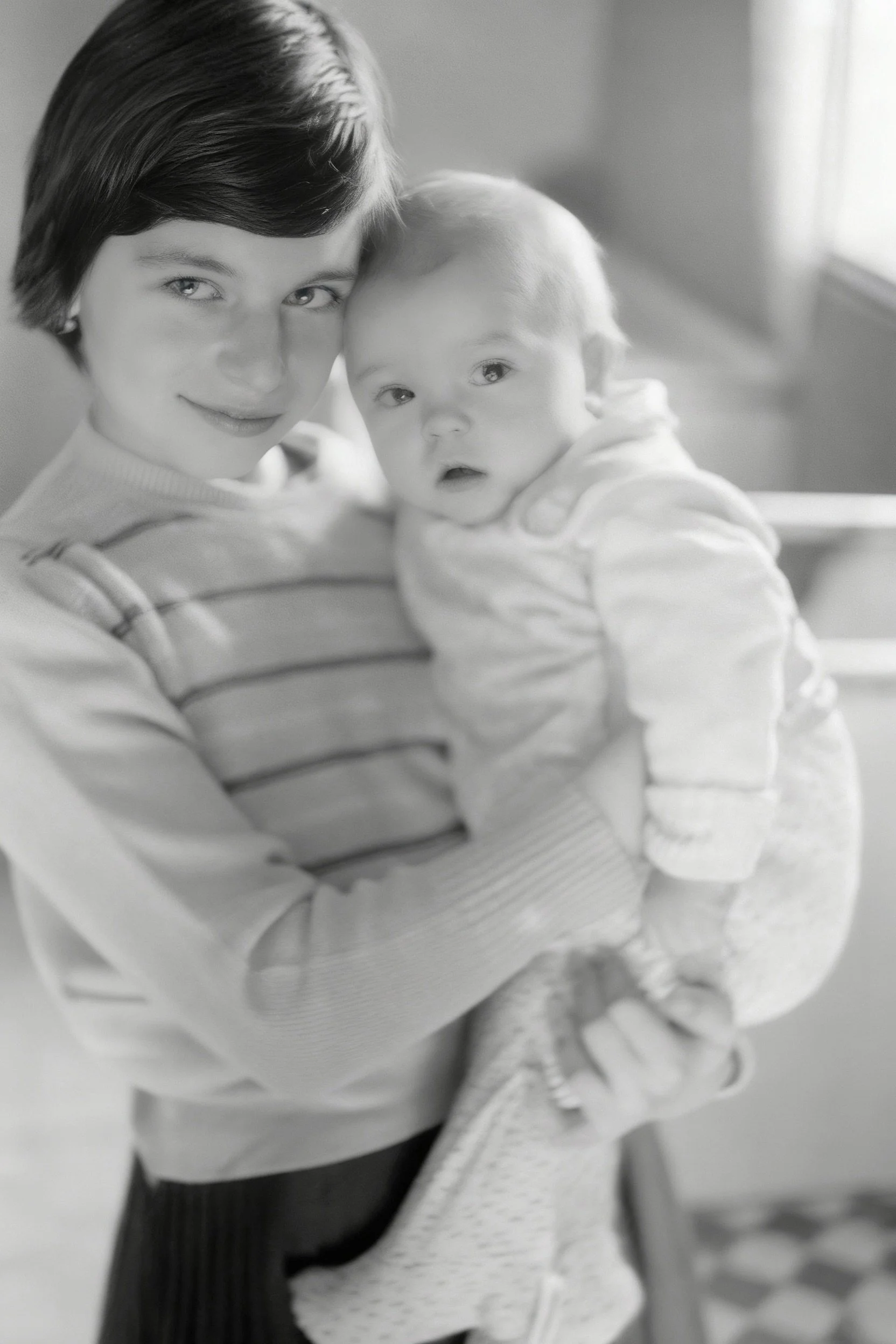 Black-and-white portrait of a woman holding a baby indoors.