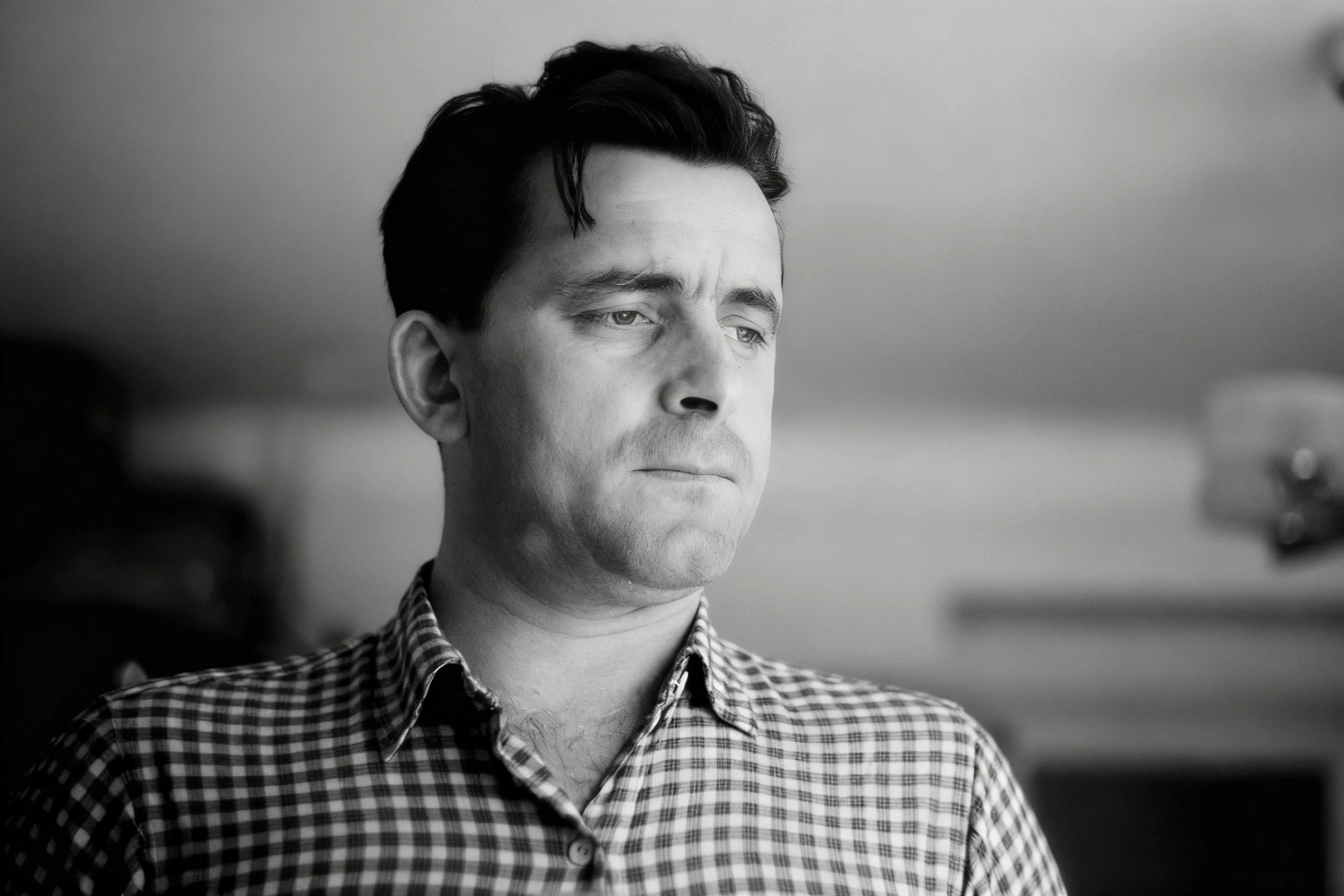 Black-and-white portrait of a man in a checked shirt looking to the side.