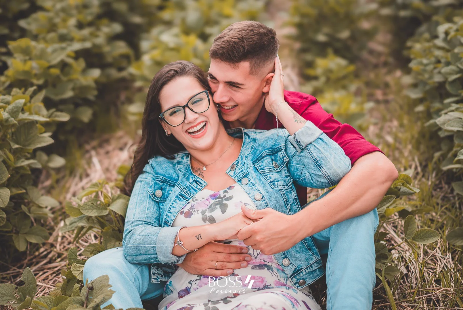 Casal sorridente e feliz, sentados na natureza, com óculos e roupas casuais, mostrando carinho e alegria.