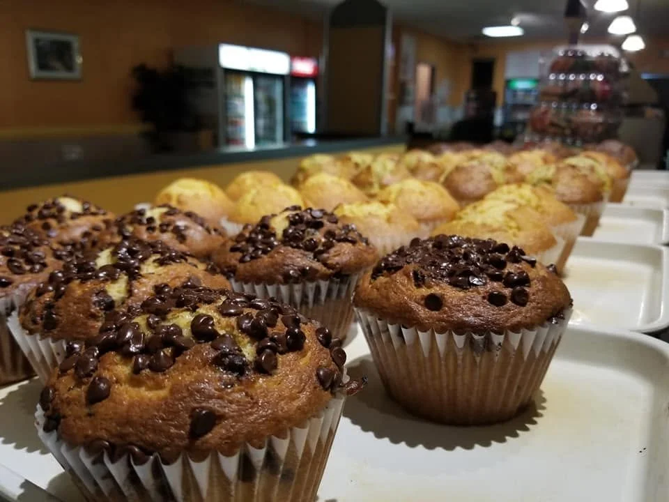 Chocolate chip muffins on a white tray in a cafe or bakery setting.