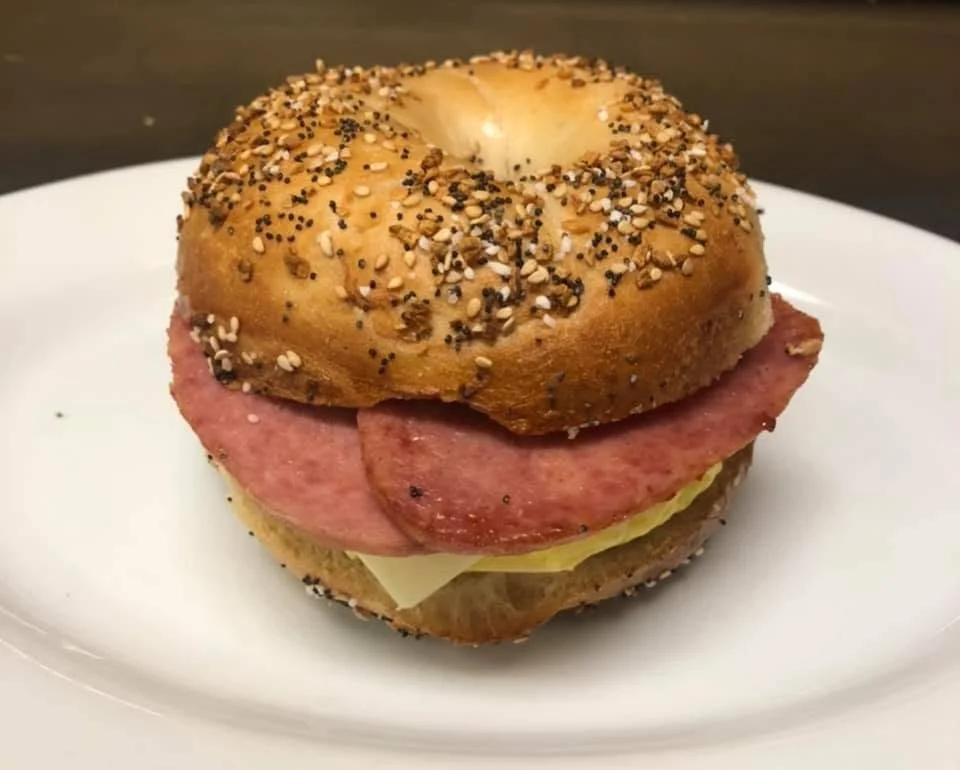 Bagel sandwich with sausage, cheese, and mustard on a white plate.