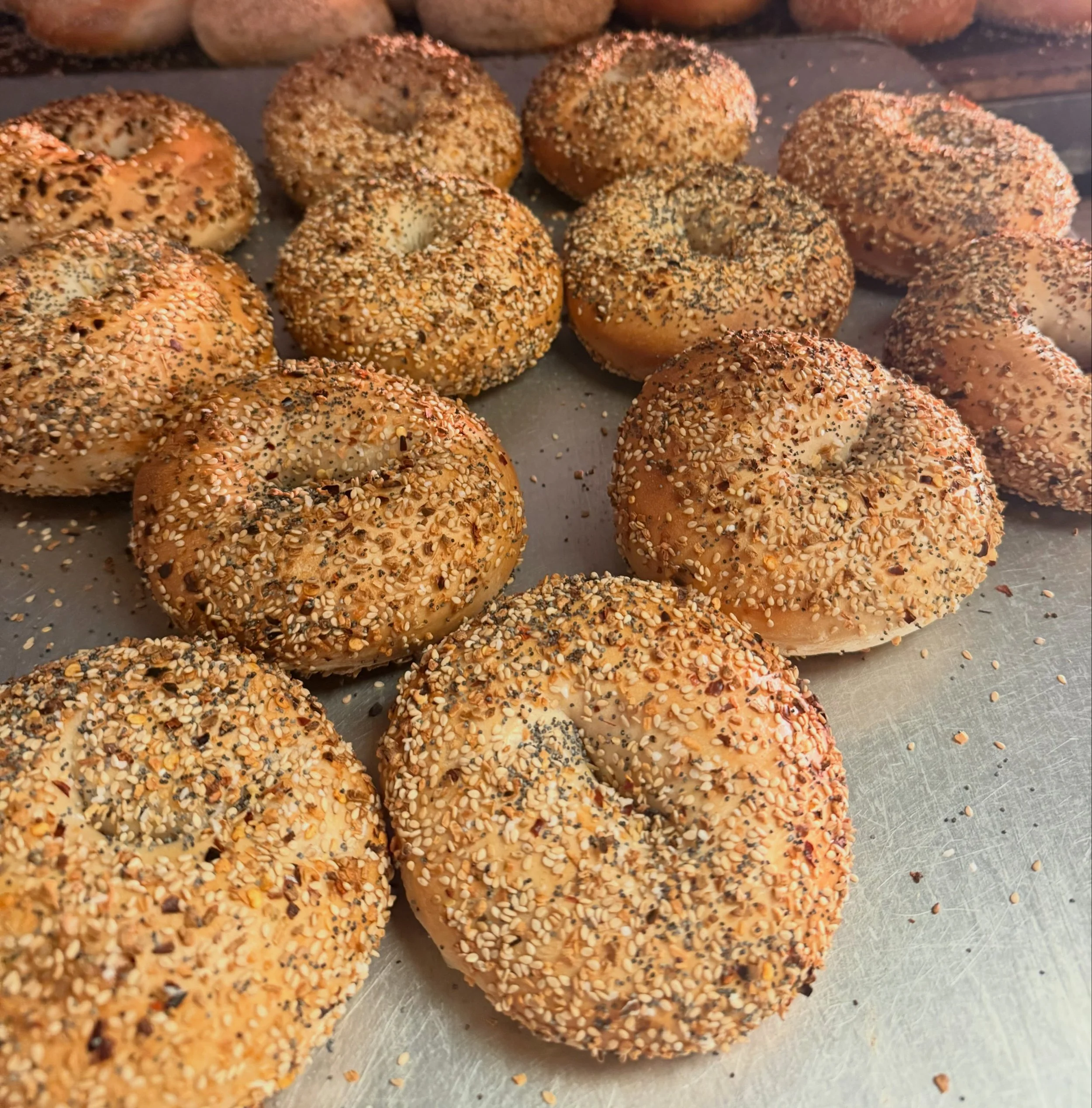 Close-up of seasoned bagel chips with sesame and black seeds on a metal surface.