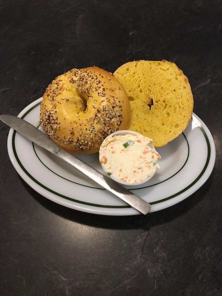 A plate with a vanilla decorated bagel, a slice of yellow cake, and a small dollop of cream cheese or frosting with herbs. A butter knife rests on the plate.
