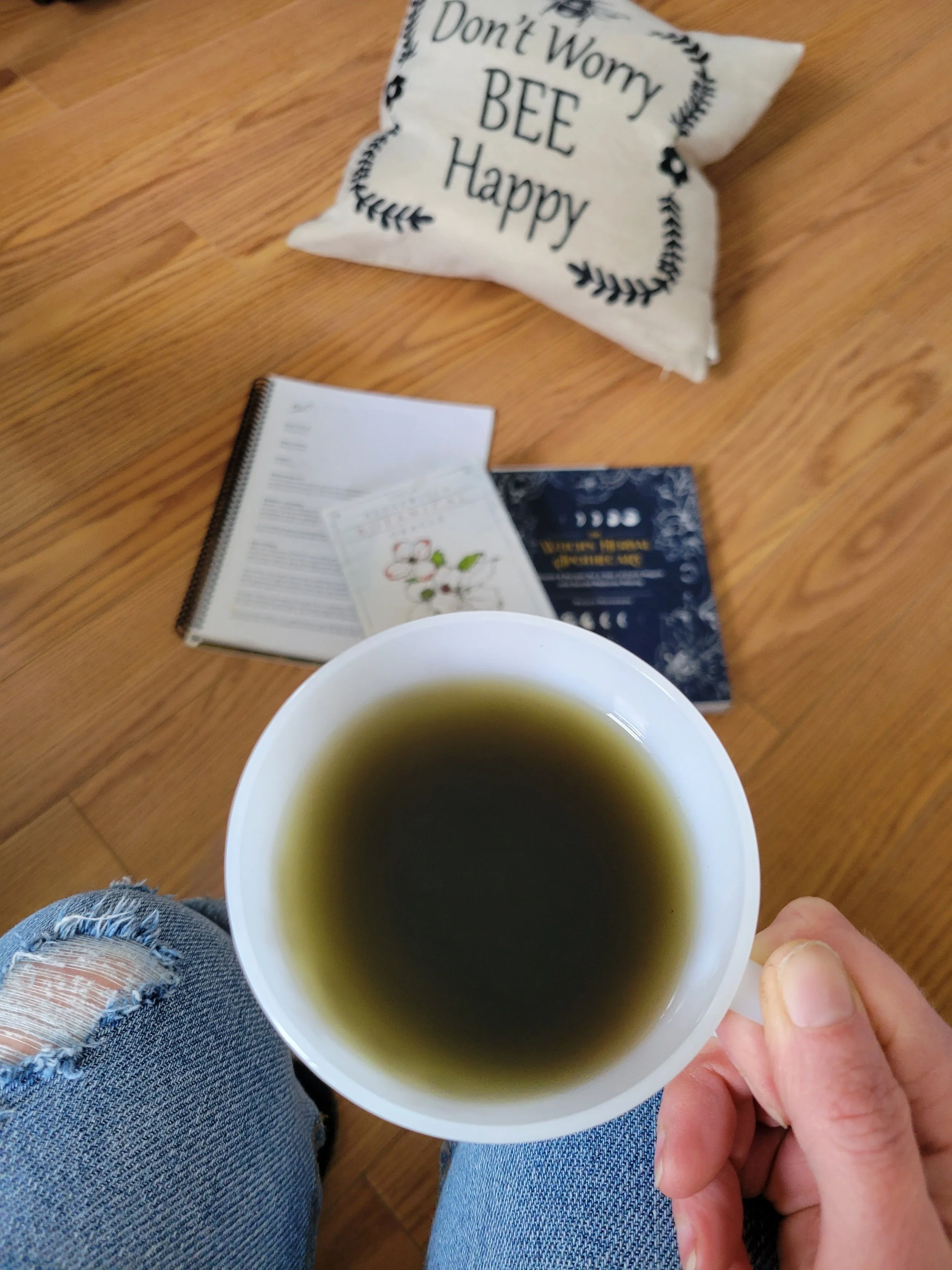 White cup of tea held over a wooden table with books and a motivational card reading “Don’t worry, be happy.”