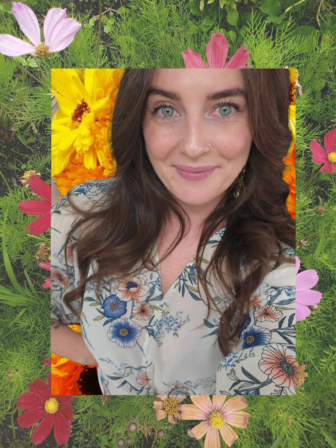 Smiling woman with long brown hair wearing a floral blouse, framed by colorful cosmos flowers and greenery