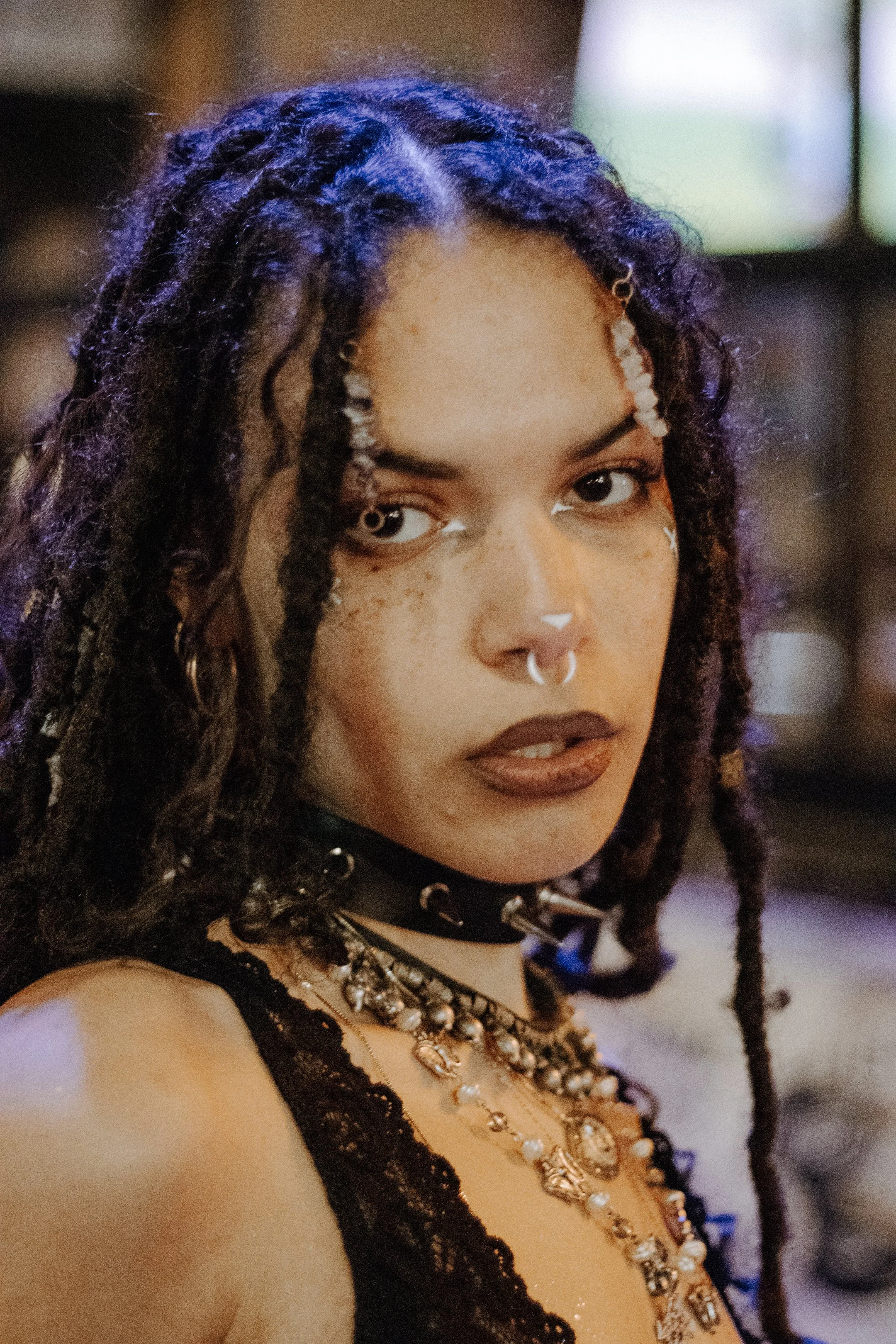 Portrait of a performer with long dark curls and a choker, holding an intense gaze