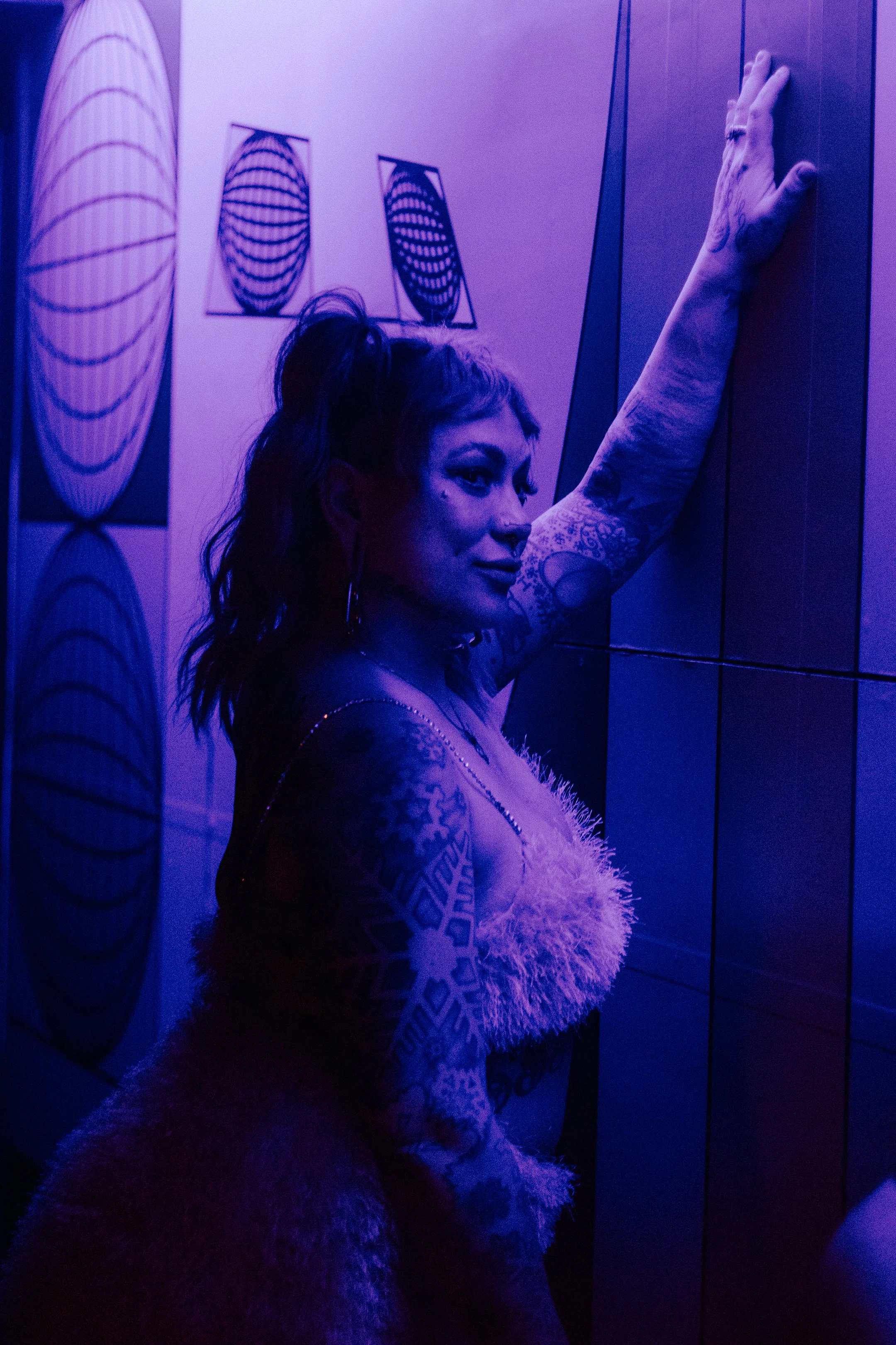 Dancer in a fuzzy textured top, arm raised high under purple club light