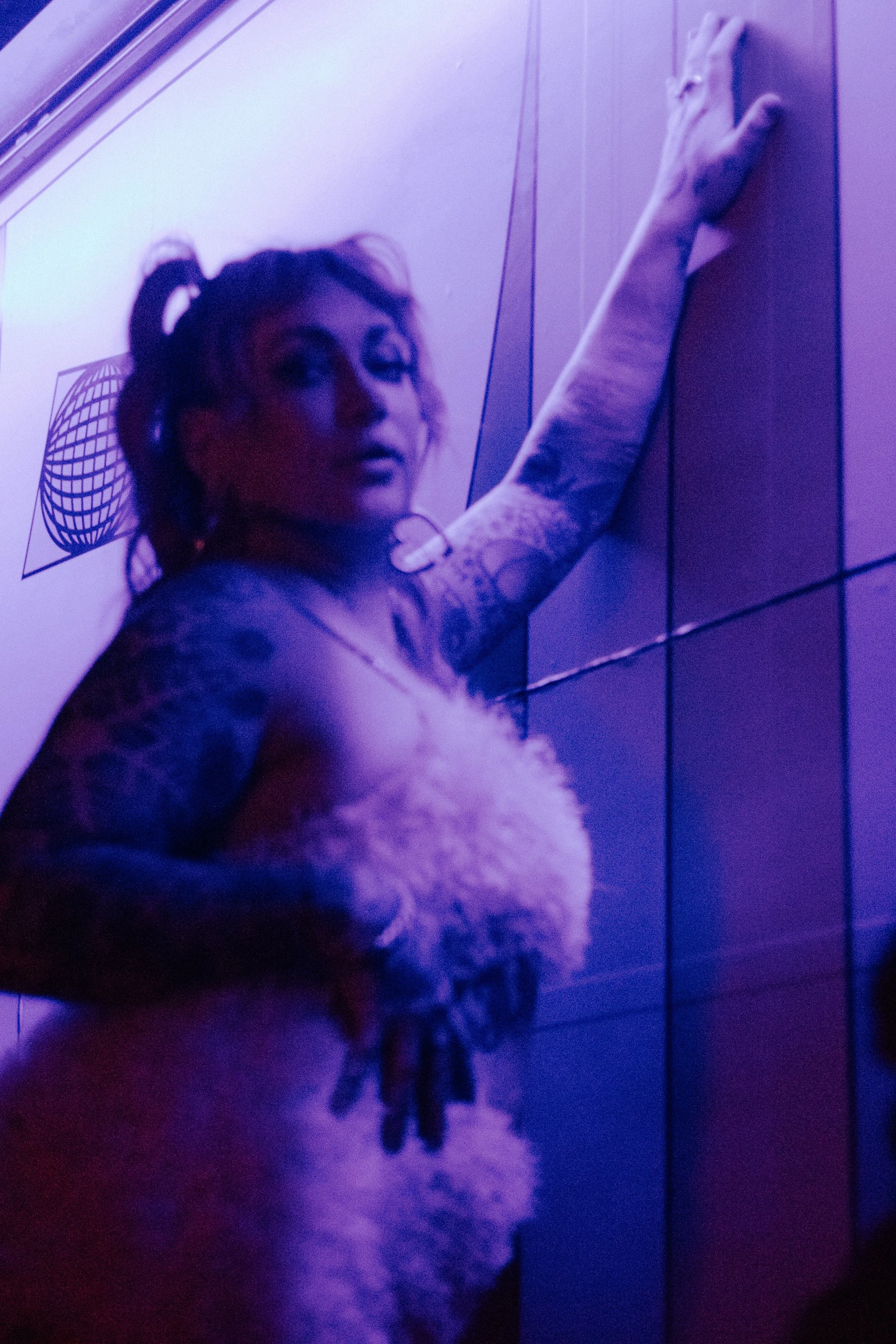Performer in a fuzzy top, arm sweeping upward through purple haze
