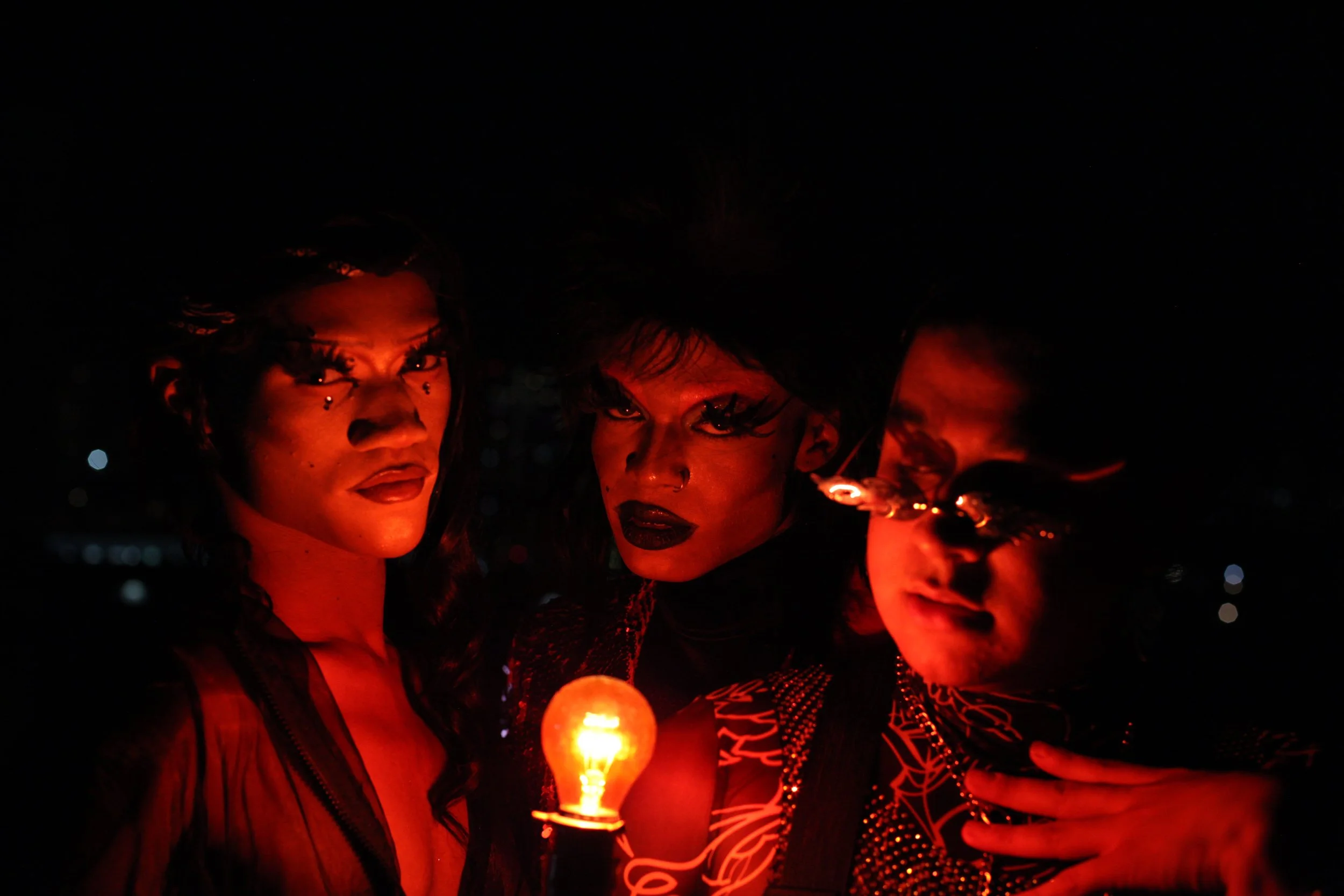 Three faces crowd around a bare bulb in the red light.