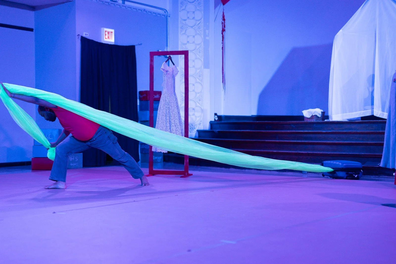 A performer stretches green fabric across a blue-lit stage in Architecture of Memory.