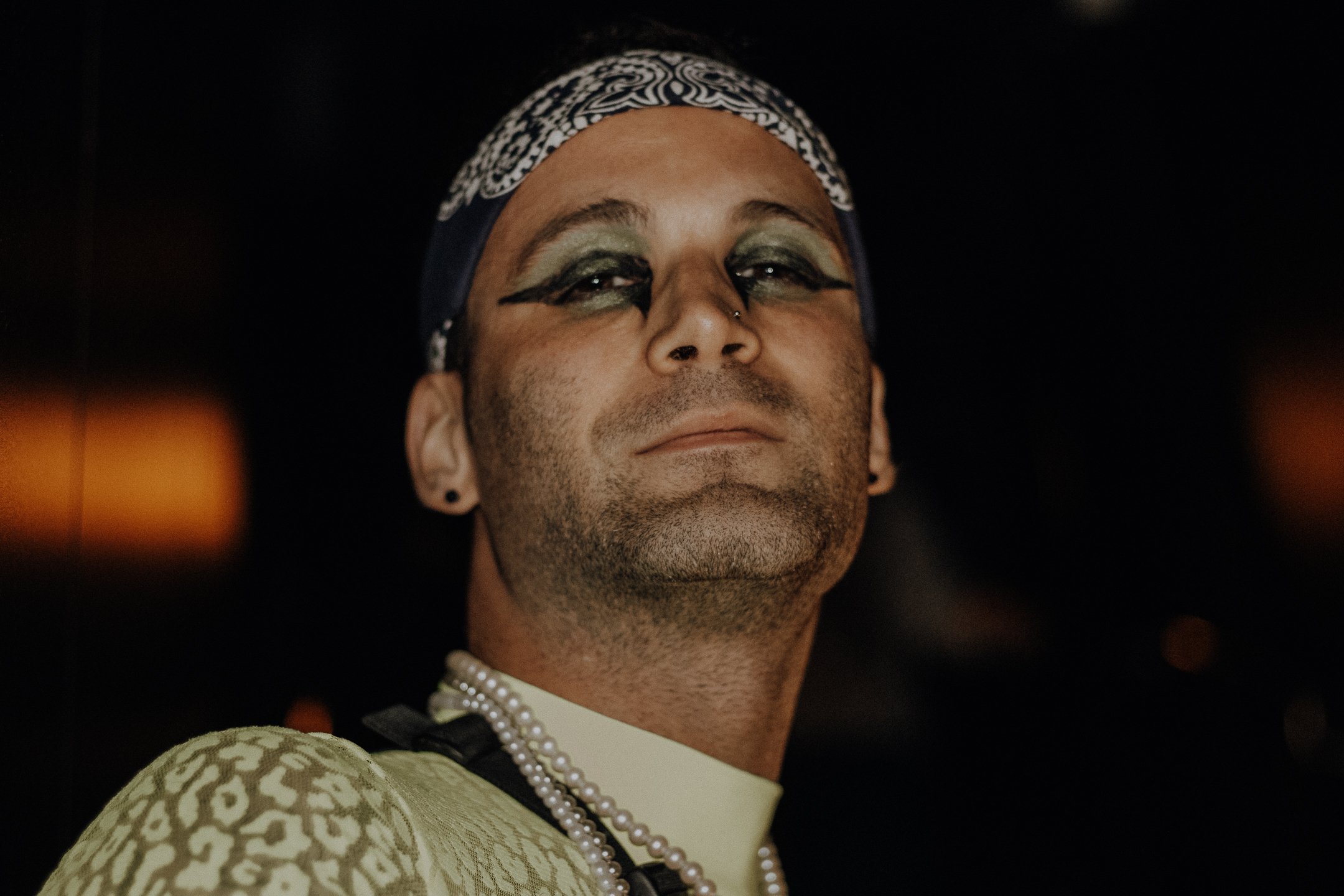 Close portrait in bandana, sharp eyeliner and a steady gaze, warm backlight glow