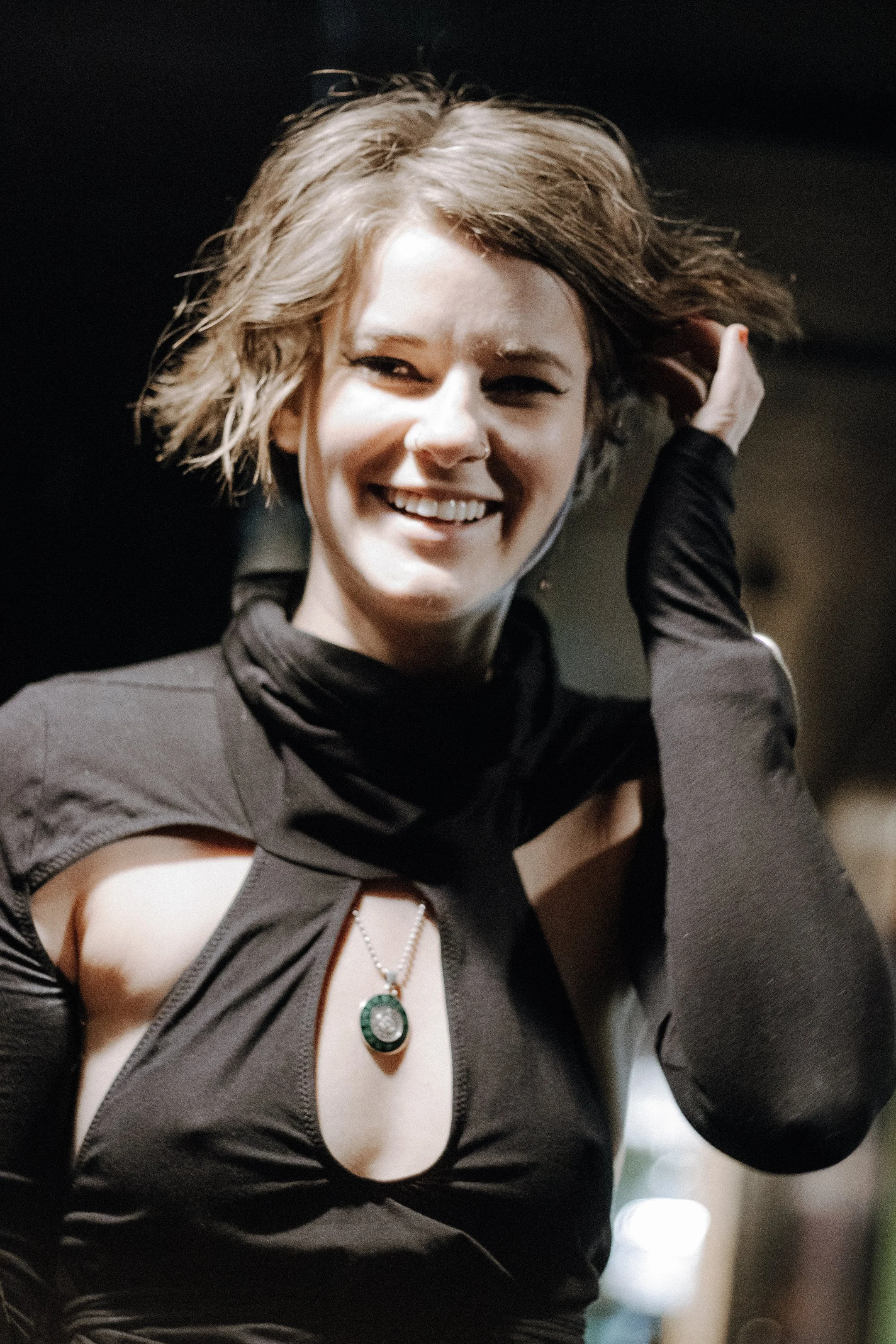 Smiling performer with short blonde hair, hand in hair, black keyhole top catching the light