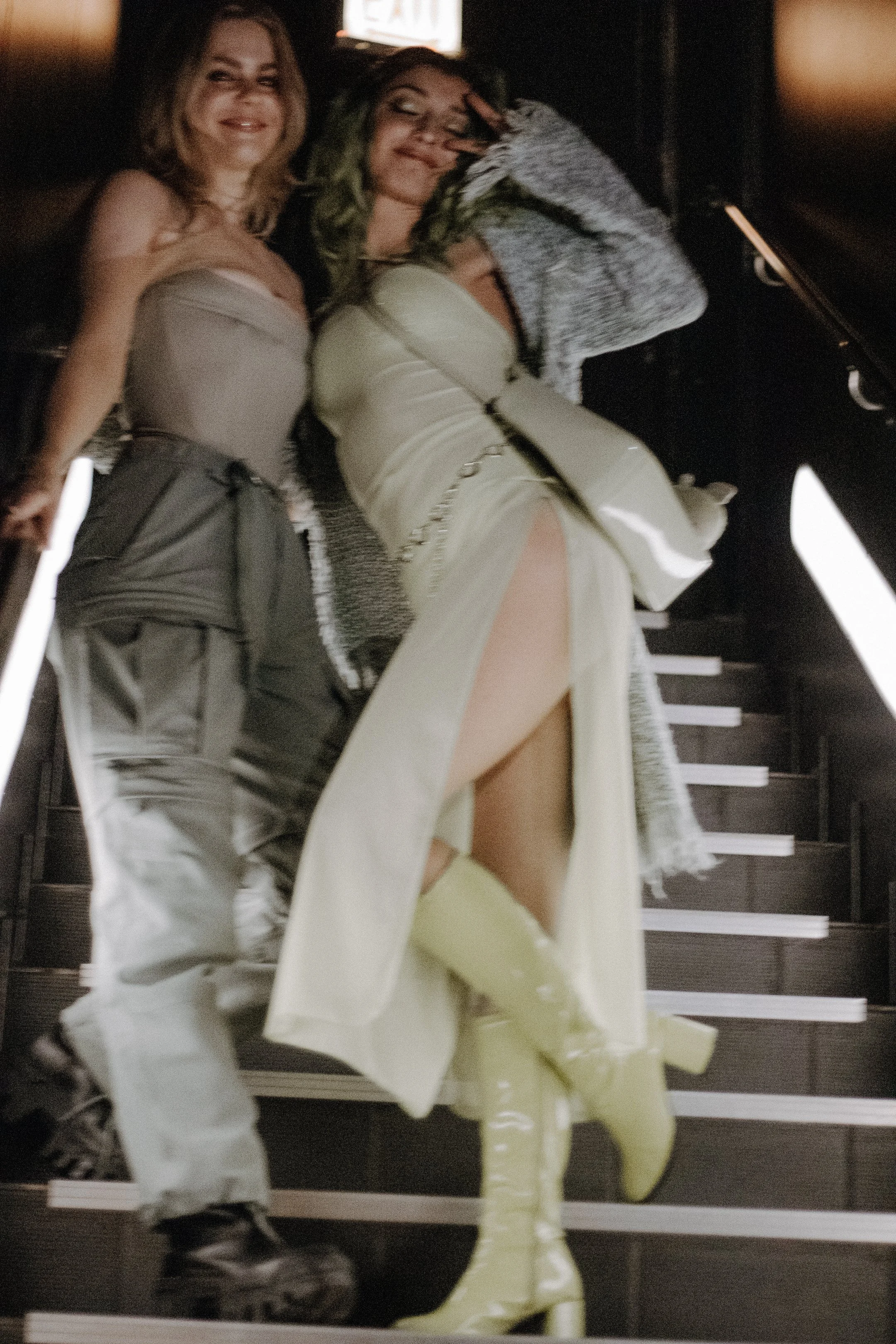 Two performers on the stairs, one in a pale dress leaning into the other