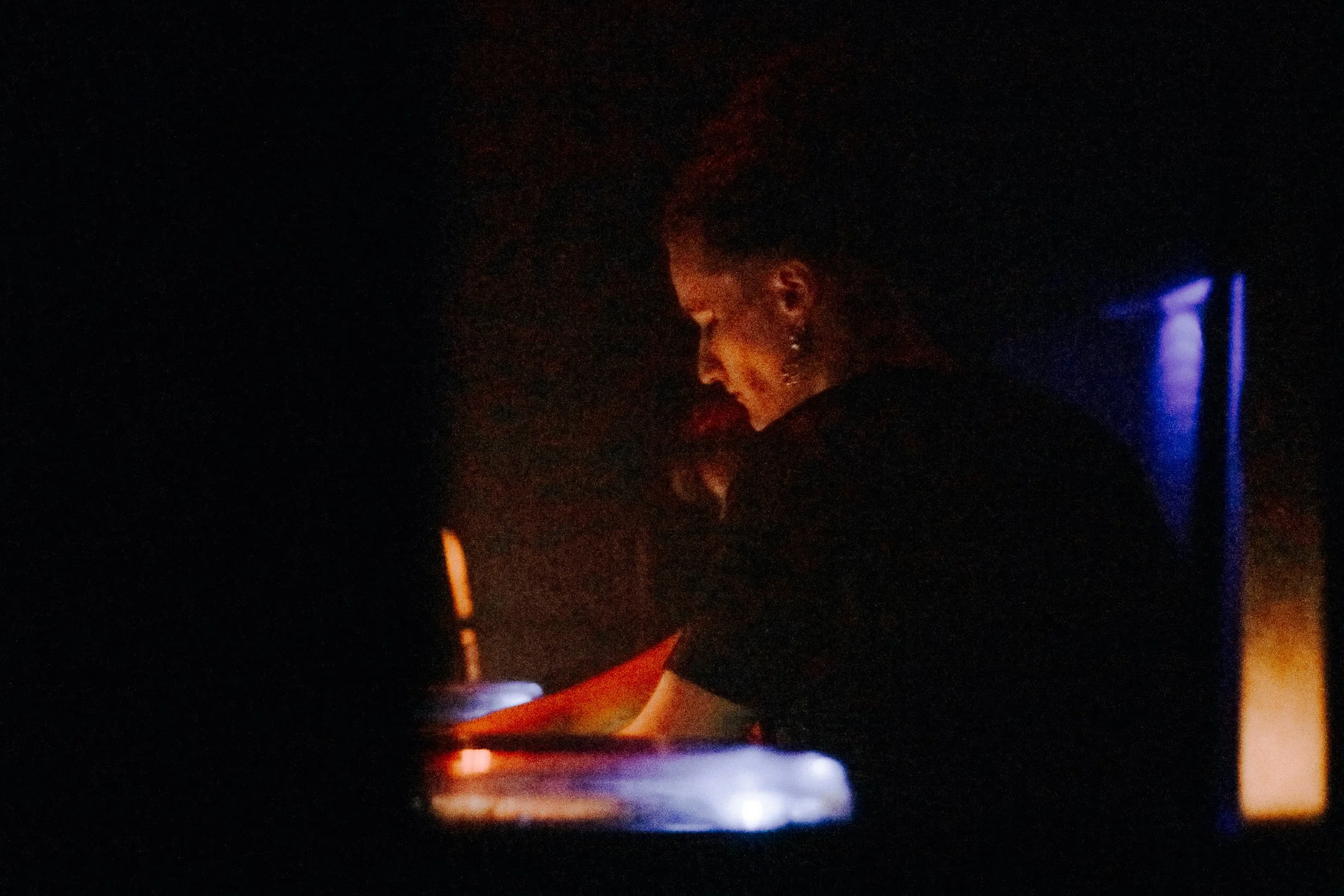 DJ silhouetted at the turntables, hands on the decks under blue club light