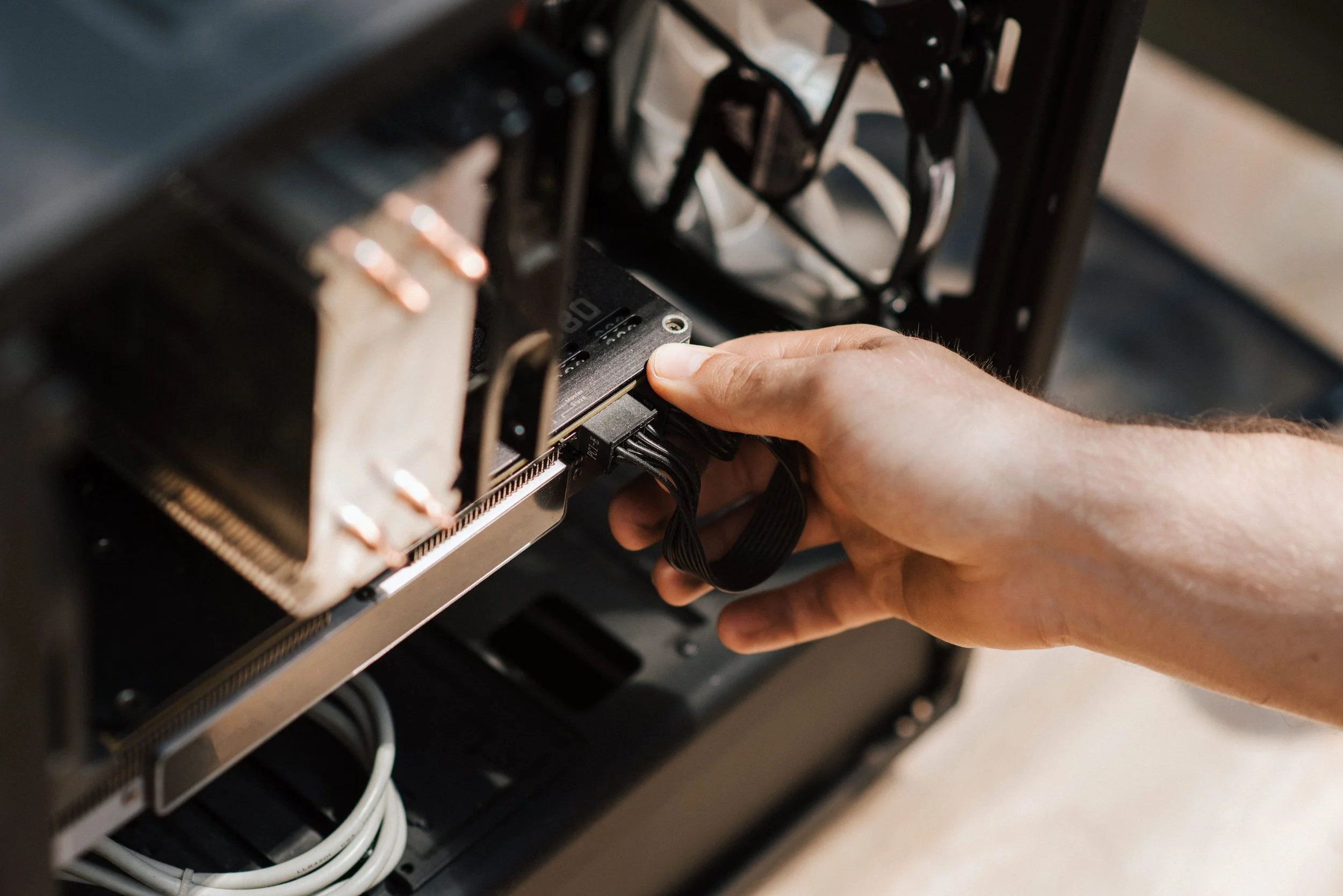 Person installing or adjusting a component inside a computer case, with visible black and white cables.