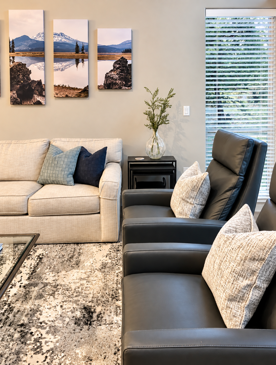 A living room with a beige sofa with blue throw pillows, black leather recliners with patterned pillows.