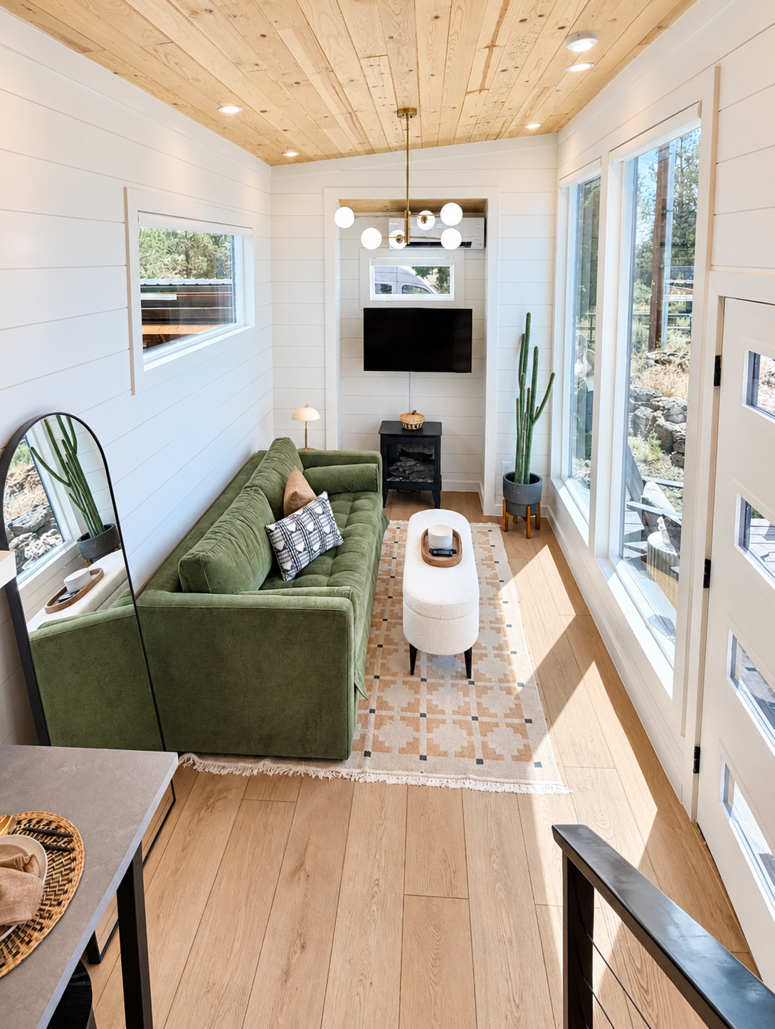 Contemporary living room with white shiplap walls, green sofa, wood ceiling, and natural light.