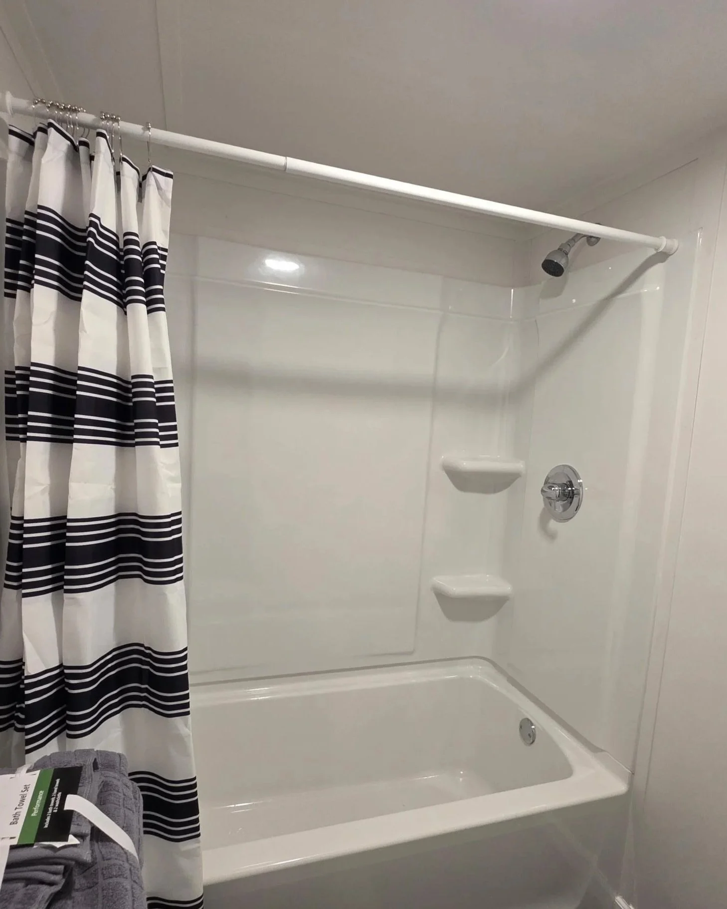 A bathroom shower area with white walls, a black and white striped shower curtain, and built-in corner shelves.