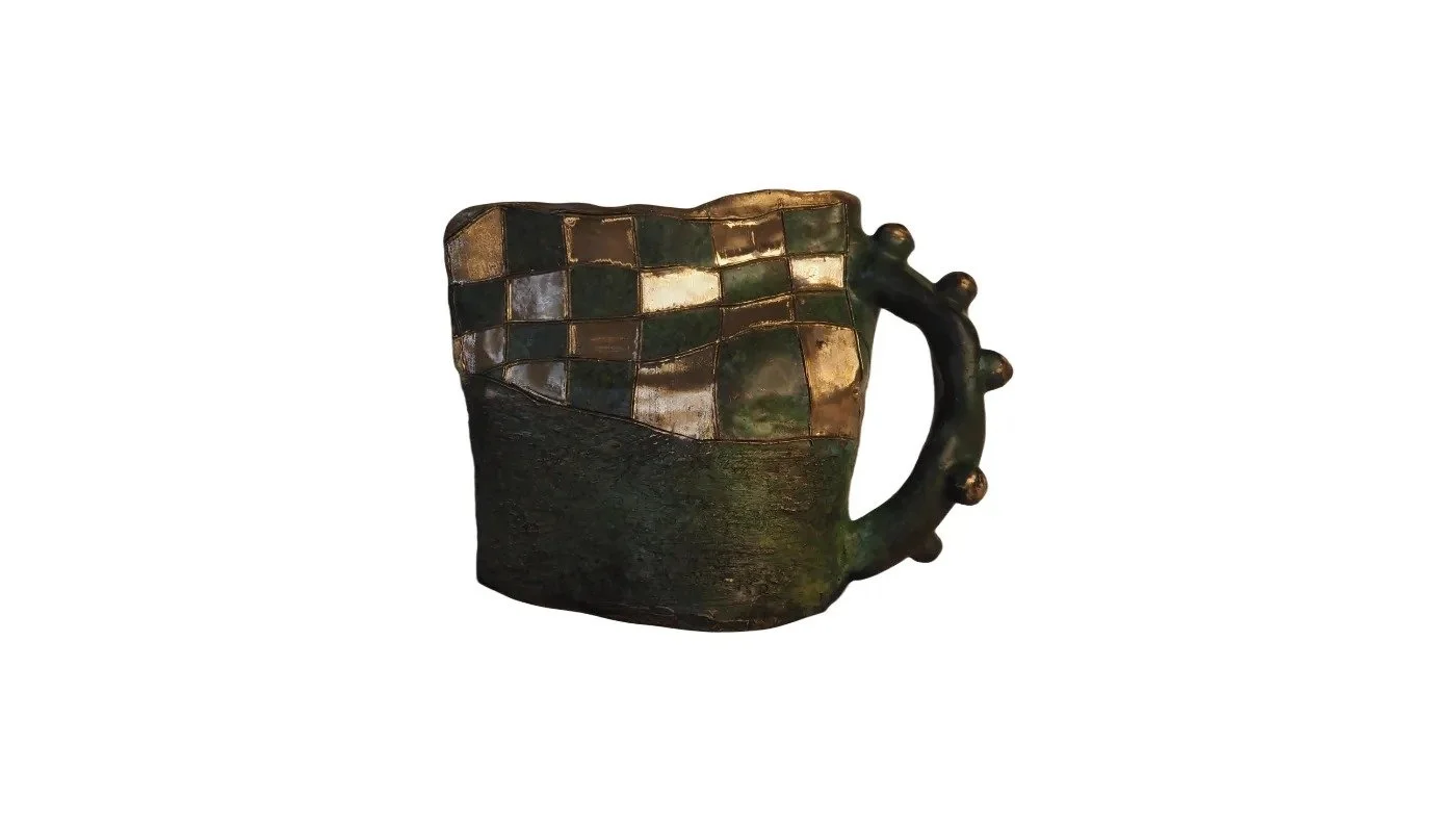 A decorative ceramic mug with a mosaic pattern on the upper half and a textured handle with round protrusions.