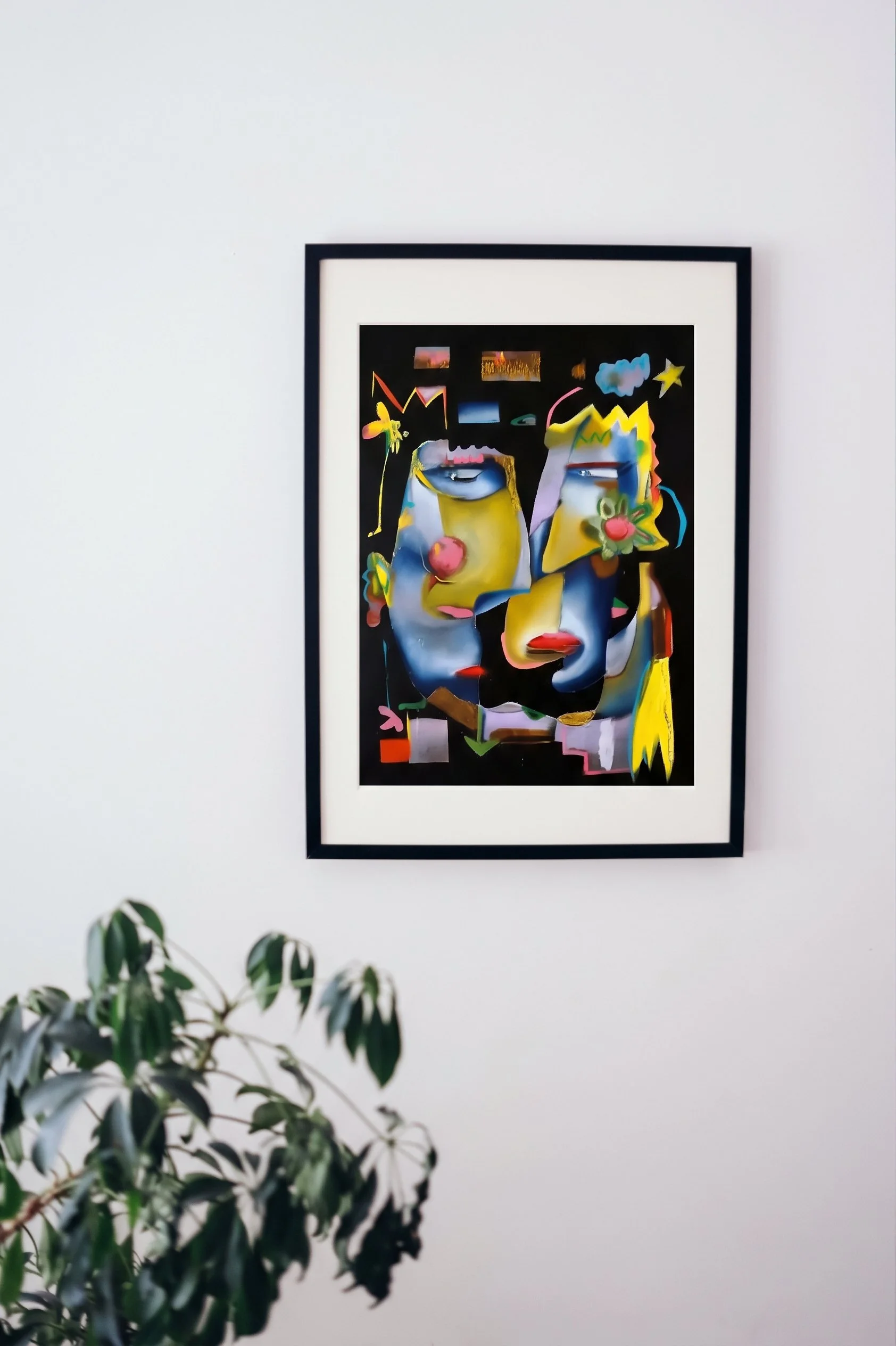 Colorful abstract portrait art hanging on a white wall with a plant in the foreground.