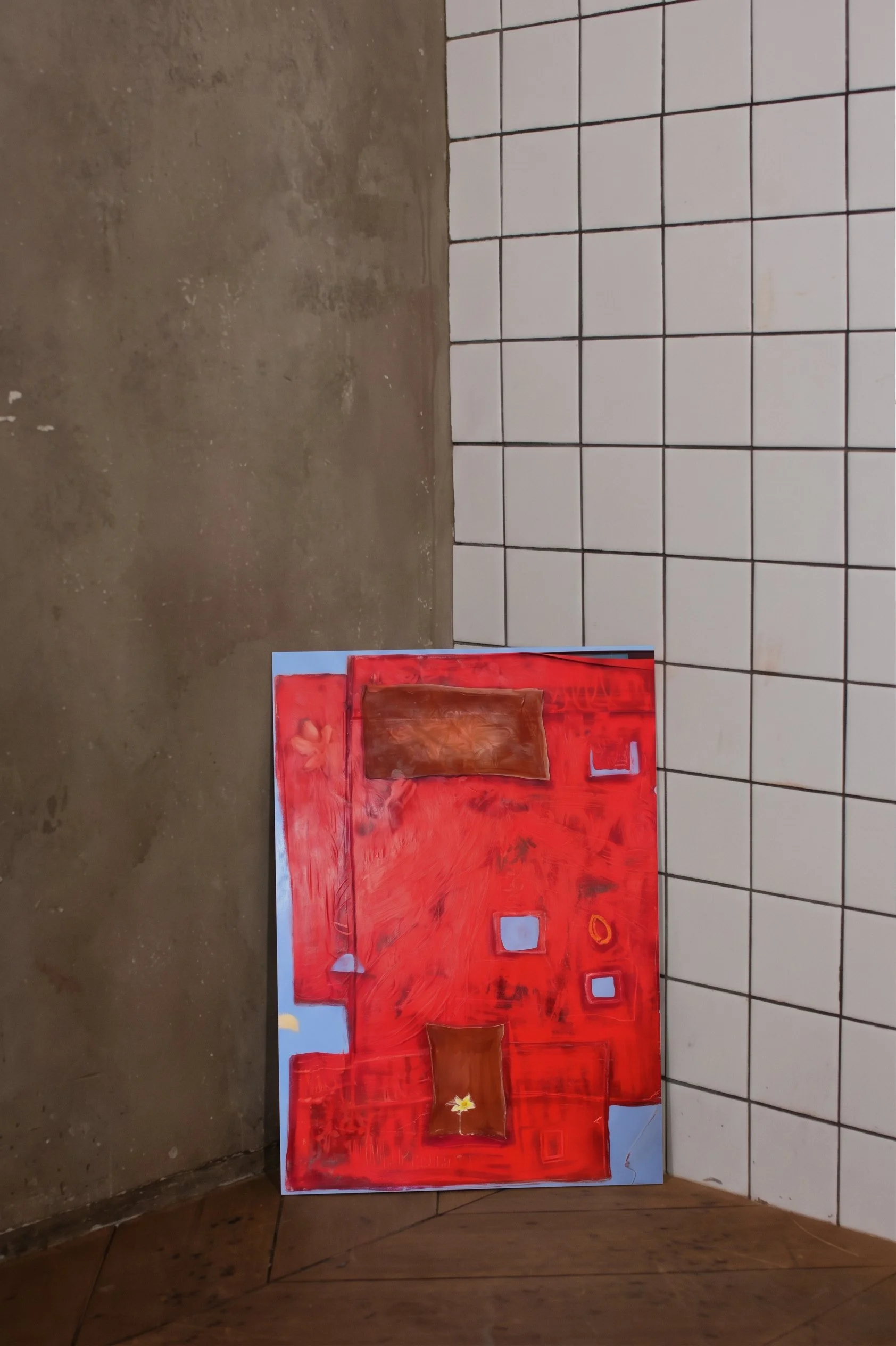 A large, colorful abstract painting with a red background leaning against a wall with white tiled section and a brown concrete floor. The painting features squares, rectangles, and a star-like shape.