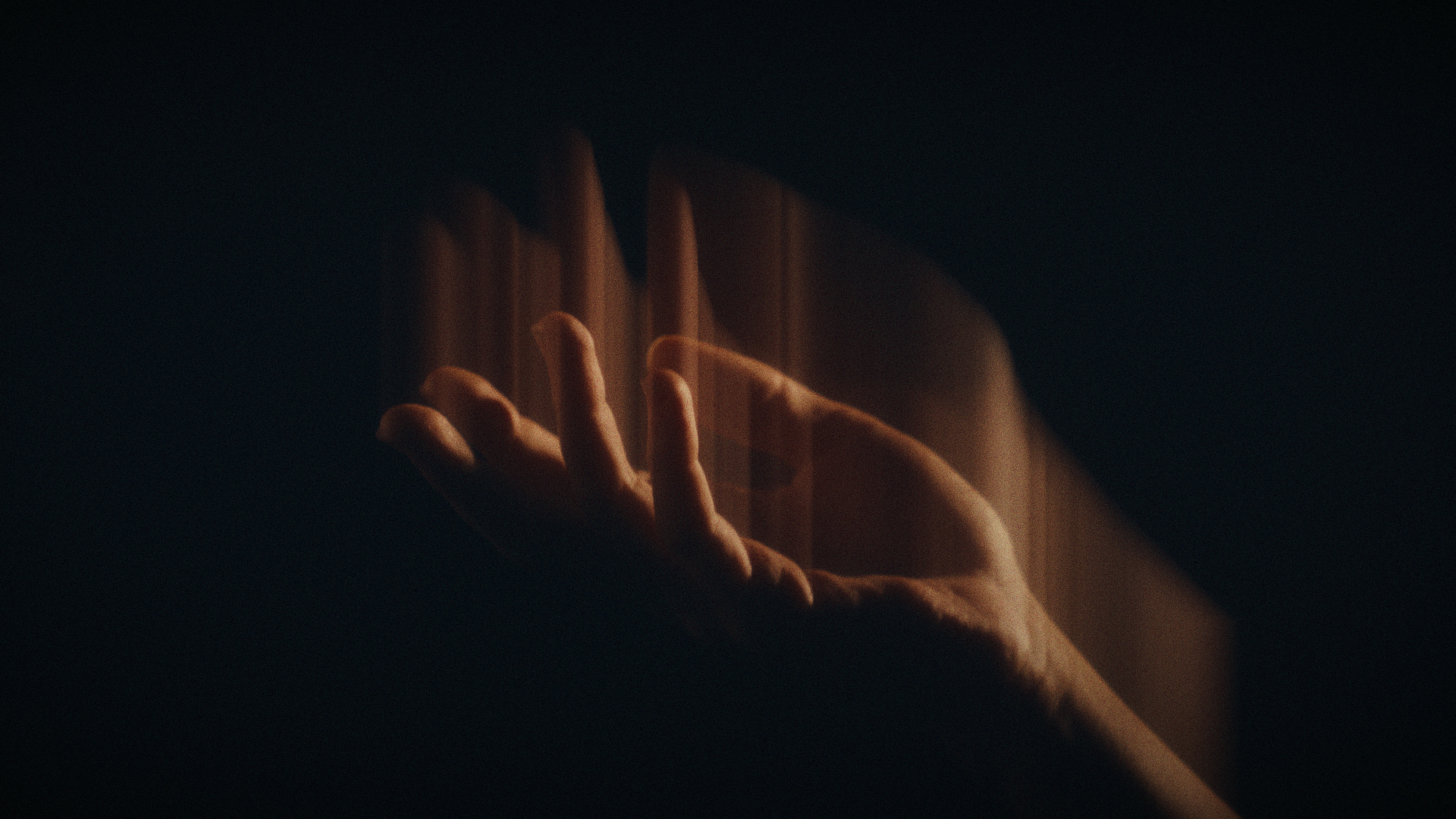 Close-up of a hand with fingers gently touching, set against a dark background with a faint glow highlighting the hand's contours.