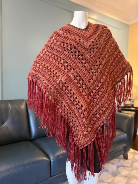 Red crocheted shawl with fringe displayed on a mannequin in a living room.