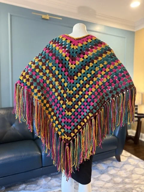 Colorful crocheted shawl with fringe hanging on a mannequin in a living room.
