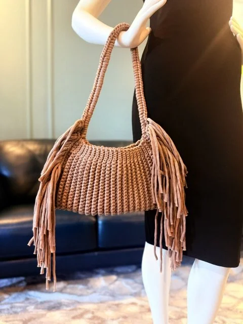 A mannequin holding a brown, knit fringe shoulder bag.
