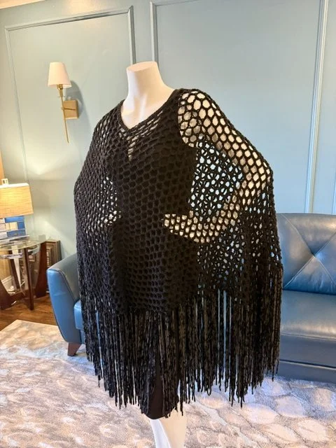 Black crochet poncho with fringe displayed on a mannequin in a living room.