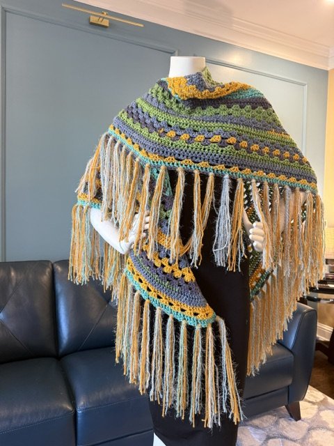 Colorful crocheted shawl with fringes on a mannequin in a living room.