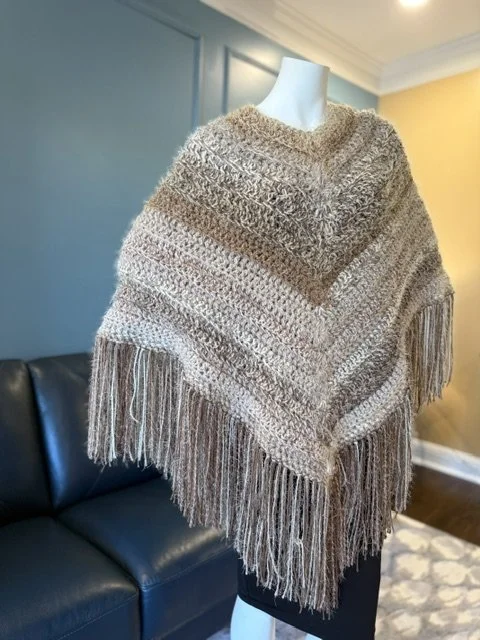 Knitted beige and brown fringed poncho on mannequin in living room.