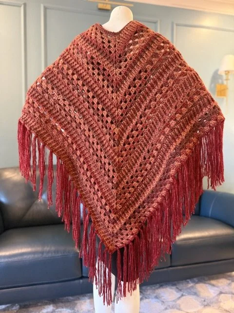Red and black knitted shawl with fringe displayed on a mannequin in a living room.