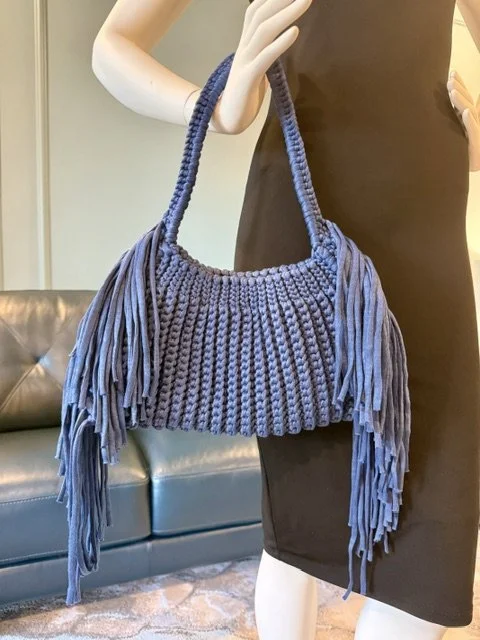Mannequin holding a navy blue, fringed, knitted handbag in a retail store.