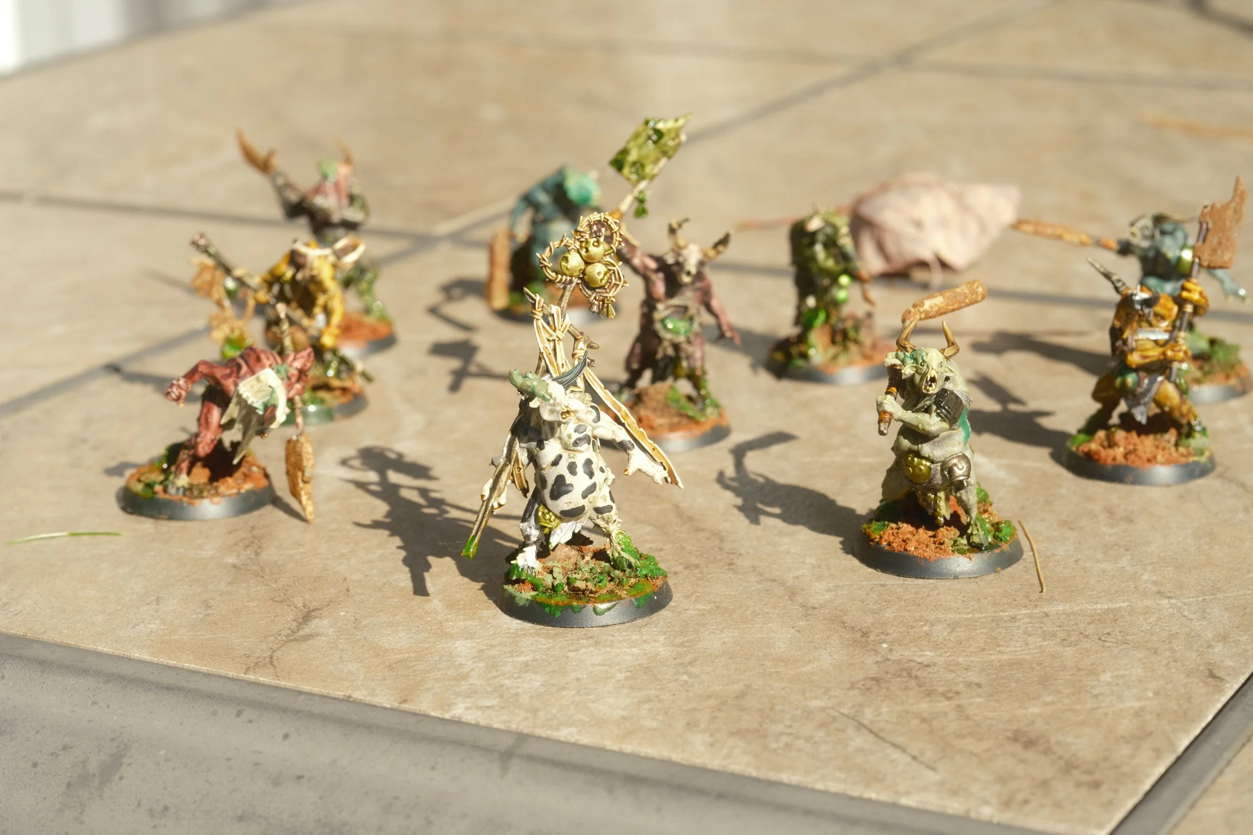 Miniatures de guerriers fantastiques peintes, représentant des créatures humanoïdes avec des armures et des armes, disposées sur une surface en pierre.