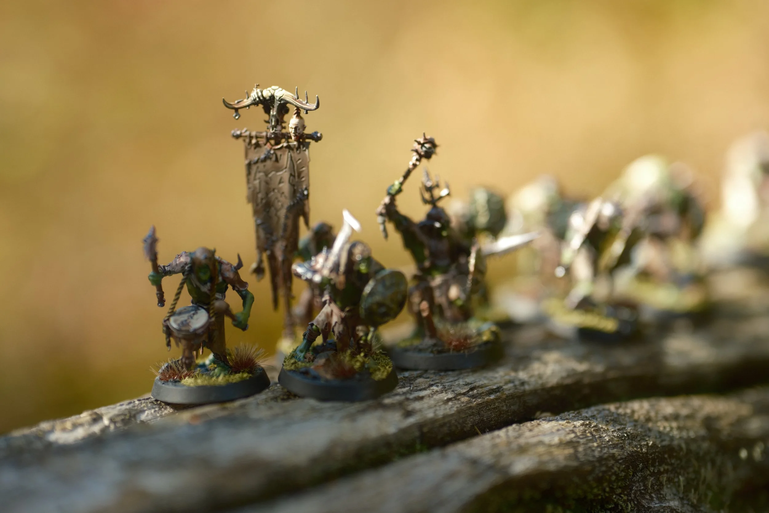 Miniatures de figurines de guerriers orks médiévaux ou fantastiques, peints avec détail, placés sur une surface en bois ou pierre, avec un fond flou beige ou brun.