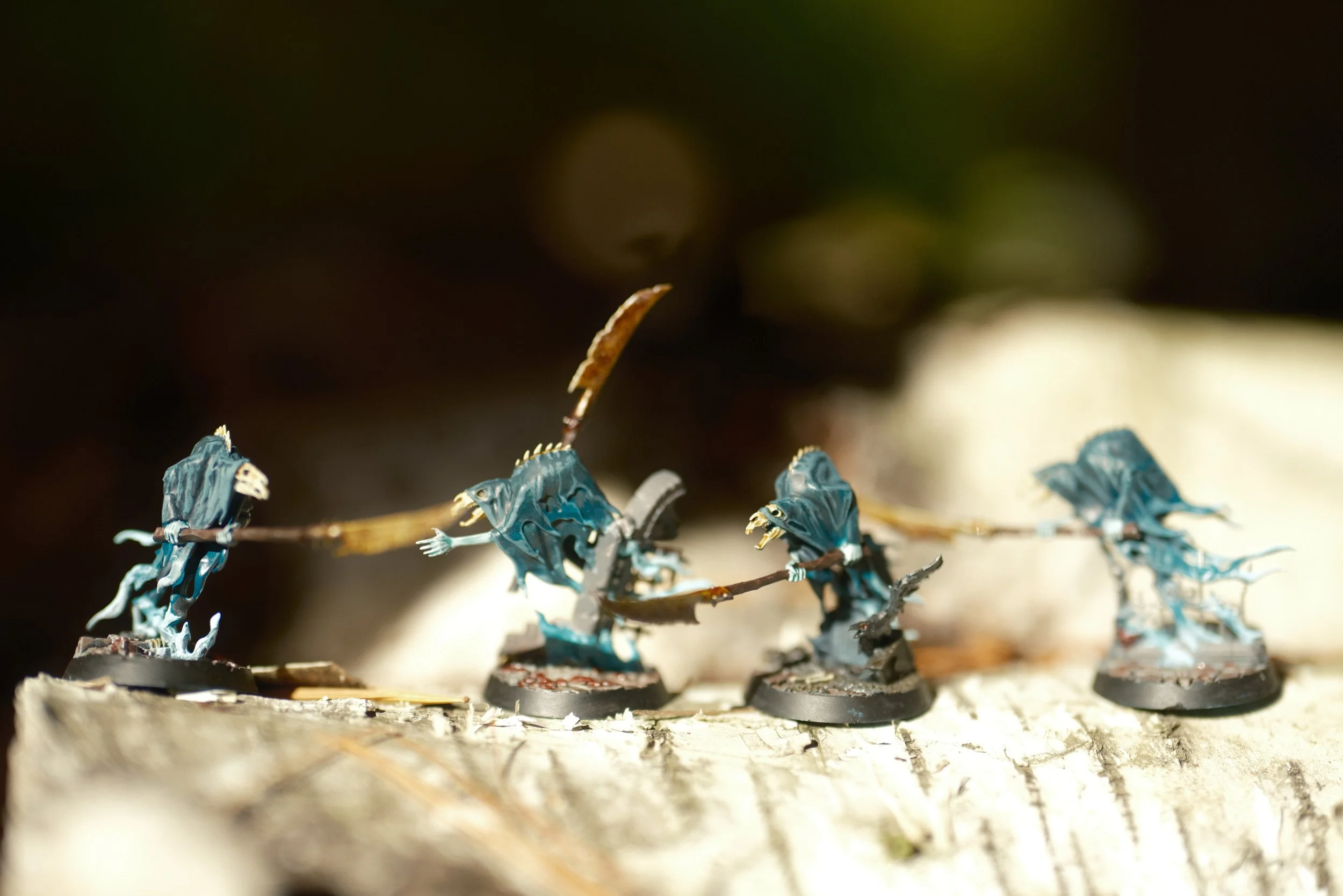 Miniatures de spectres en combat, peintes à la main, disposées sur une surface en bois ou en pierre.