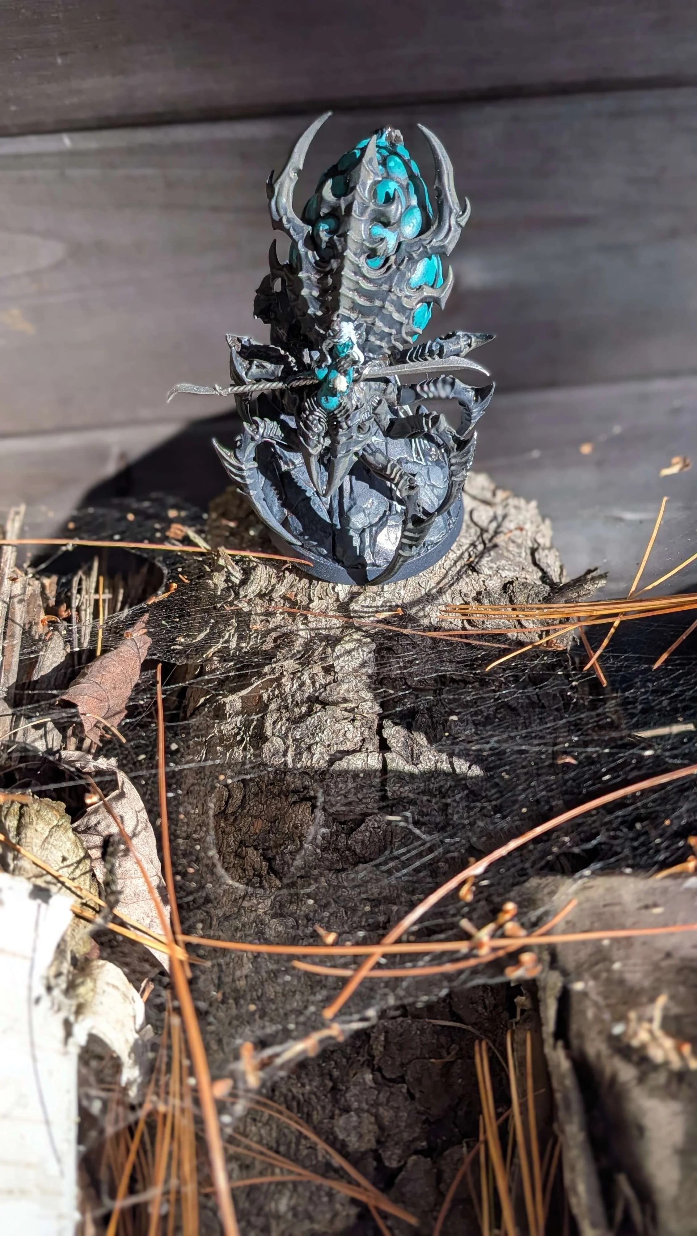 Une figurine d'araignée noir avec des accents bleus, placée sur une souche d'arbre dans la nature.