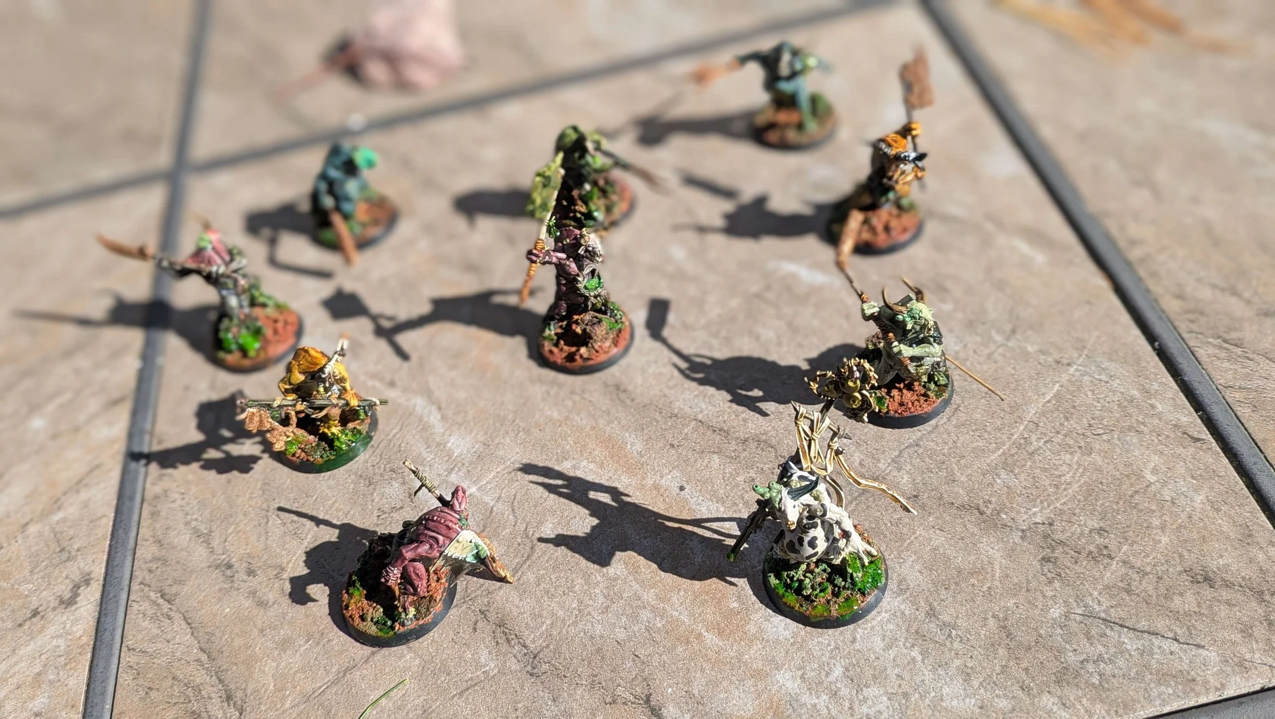Miniatures de guerriers et créatures fantastiques peintes, disposées sur une surface en pierre, utilisées pour un jeu de rôle ou de stratégie