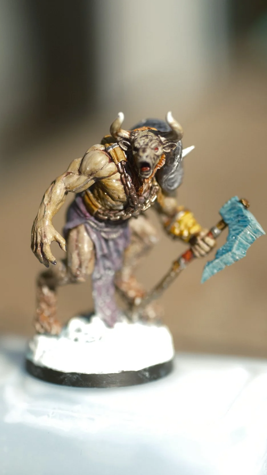 Figurine de créature fantastique (minotaure) avec un corps musclé, une tête de taureau, un bâton avec une hache, et une chaîne noire autour du cou.