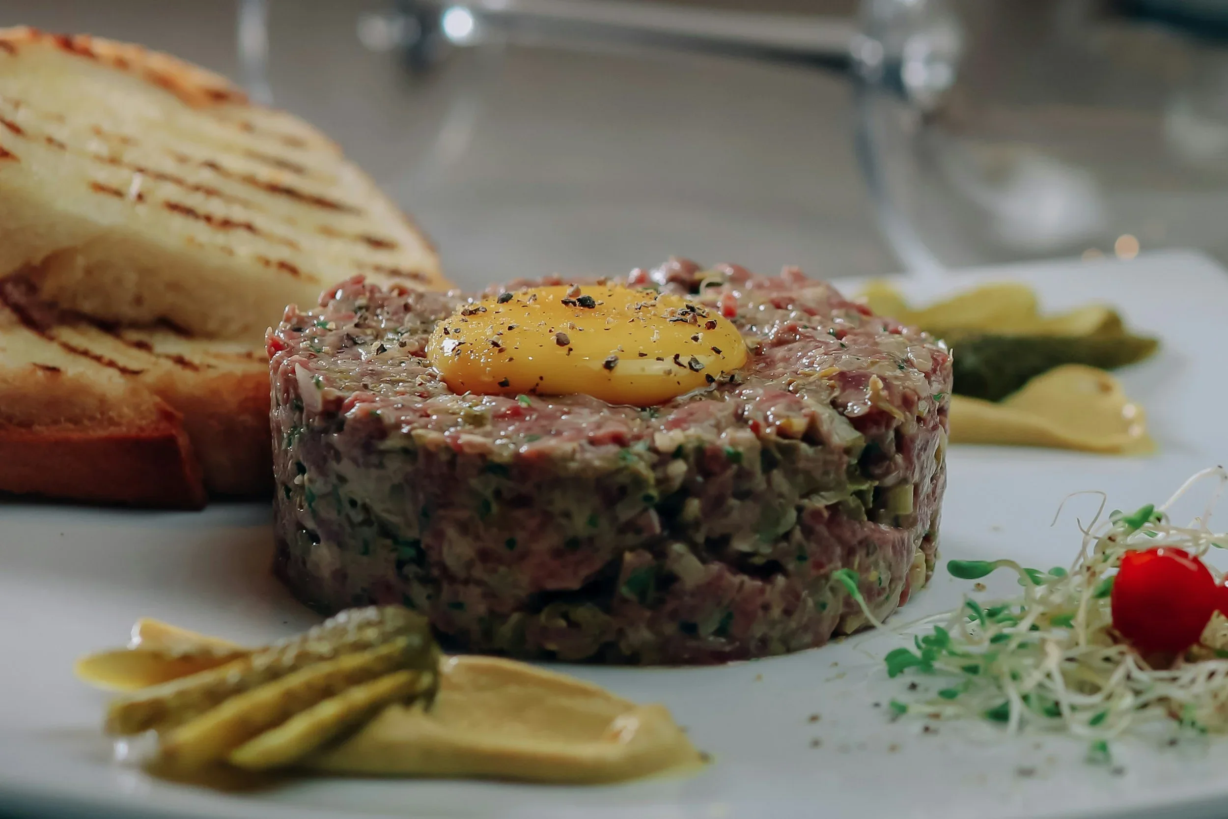 A plate of steak tartare topped with a raw egg yolk, served with grilled bread and side salad.