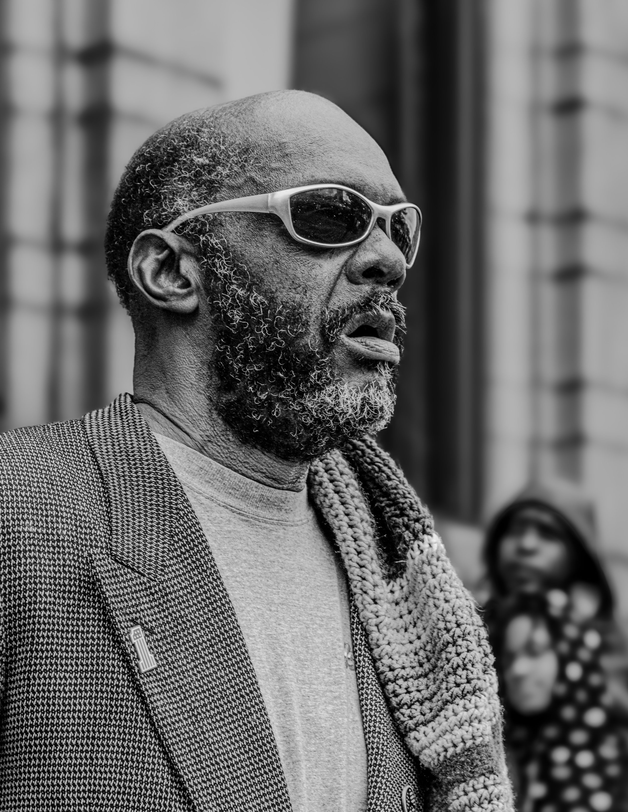 Black-and-white portrait of a bearded man wearing sunglasses and a textured jacket, looking to the side.