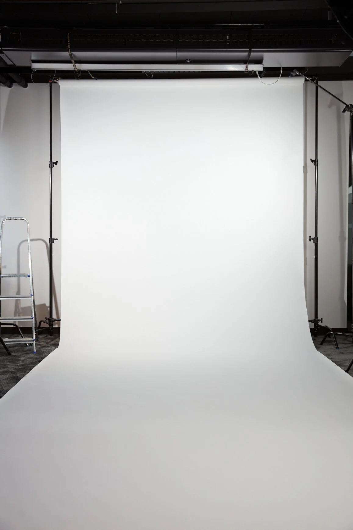 En vit bakgrund för fotografering i studio med ställningar och trappa på sidorna.