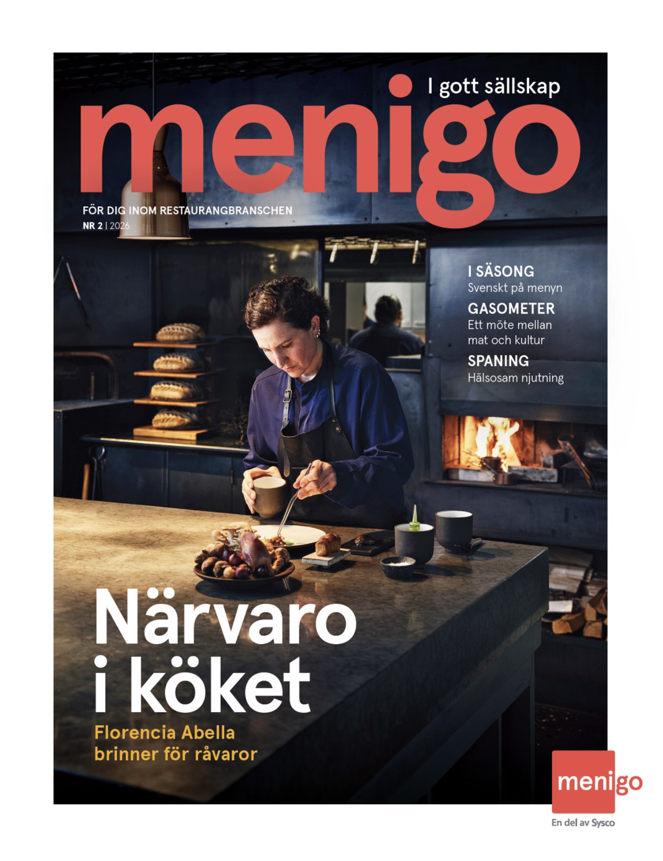 En kvinna i ett kök, som förmodligen är kock, står vid ett köksbord med mat och dryck, i bakgrunden en öppen spis. Kotletter, bröd och andra råvaror är synliga på bordet. Läser tidningen "menigo" med rubriken "Närvaro i köket".