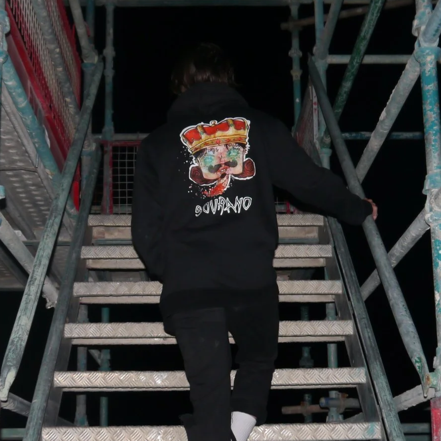 Person wearing a hoodie with a clown face and crown graphic on the back, ascending metal stairs at night.