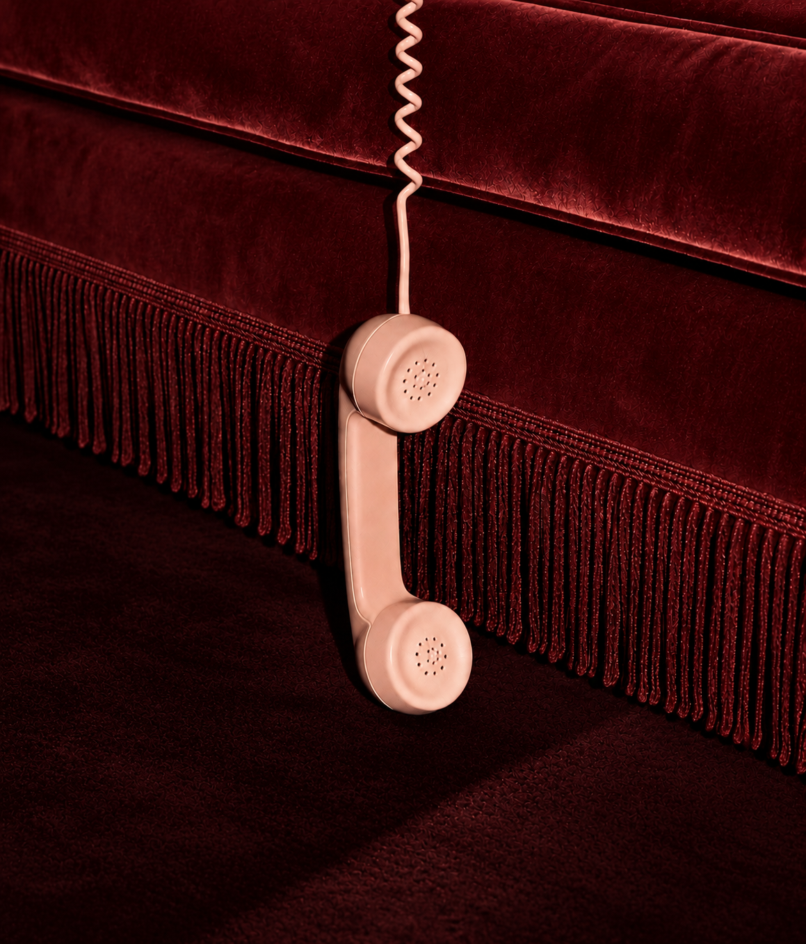 A beige vintage-style telephone hanging on a red velvet couch with fringed trim.
