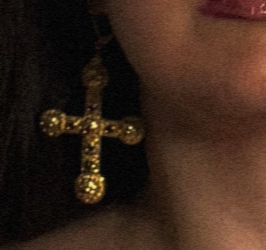 Close-up of a gold cross earring worn on the ear, with part of a person's face and red lipstick visible.
