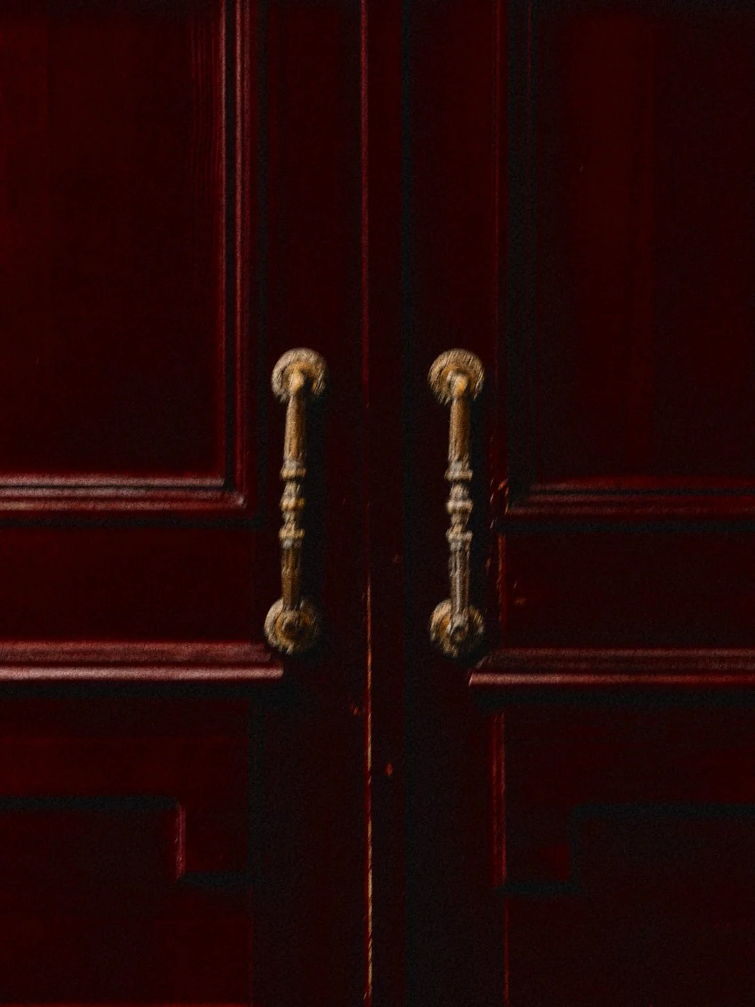 Close-up of dark red wooden cabinet doors with ornate gold handles.